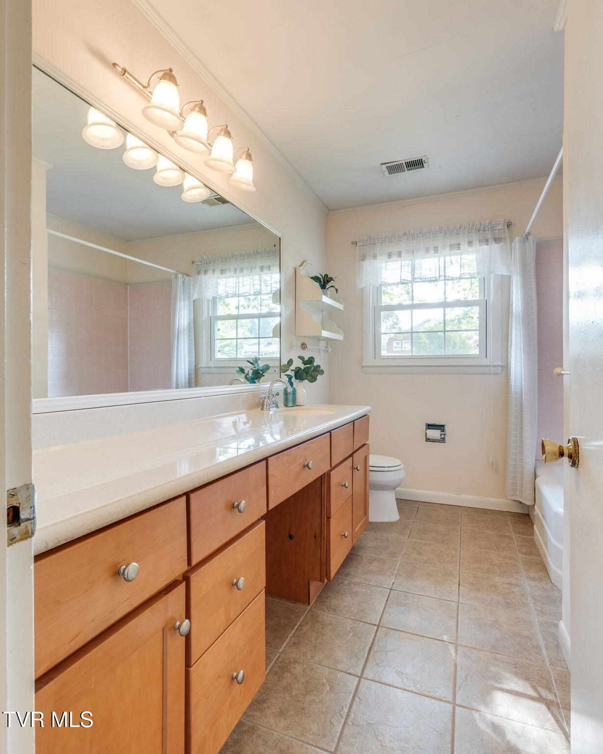 Bathroom with a long wood vanity, large mirror, and window beside the tub and toilet.