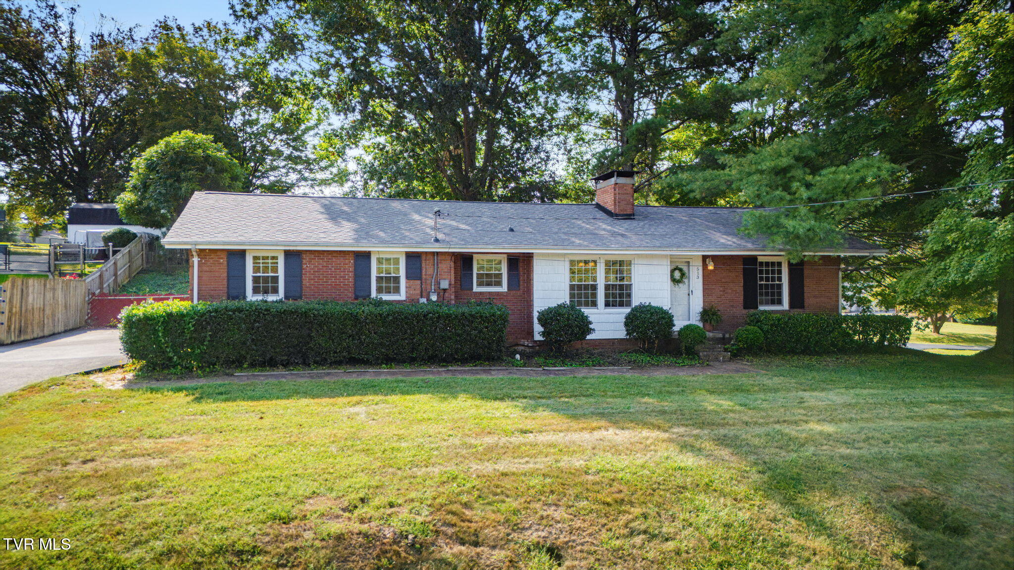 Single-story brick ranch with white siding, a trimmed front hedge, and mature trees.