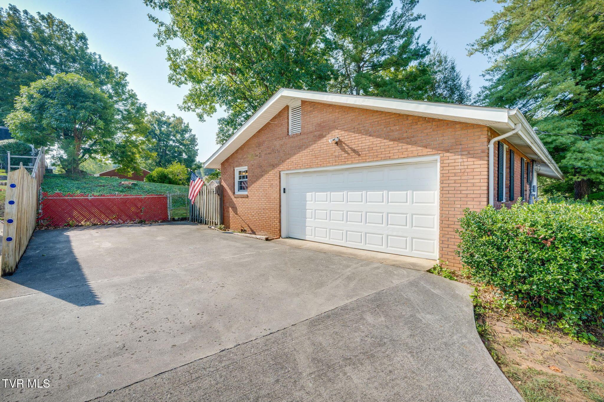 Brick house with a white double garage door and broad concrete driveway beside a fenced yard.