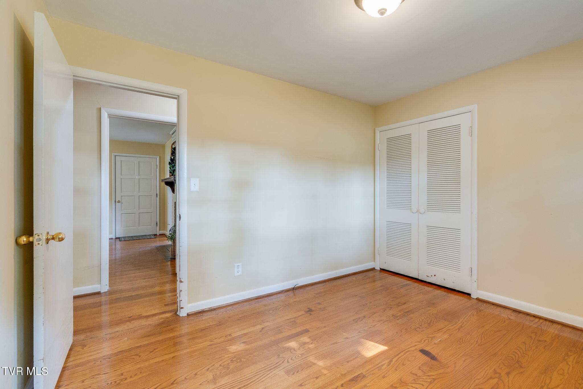 Empty room with hardwood floors, beige walls, and a white louvered closet.