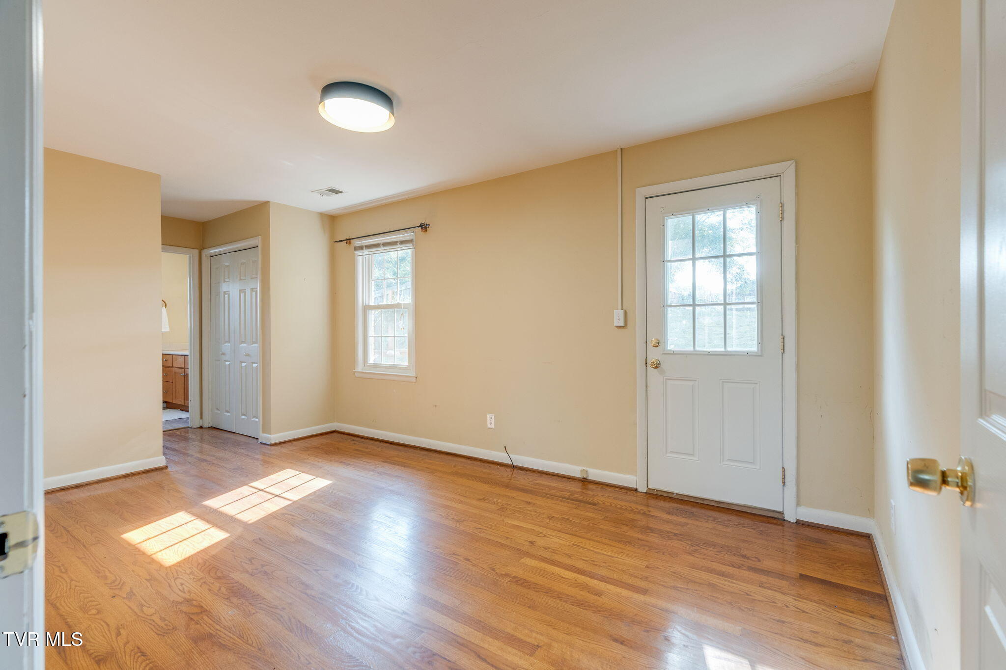Empty room with hardwood floors, tan walls, a window, and a white glass-paneled exterior door.