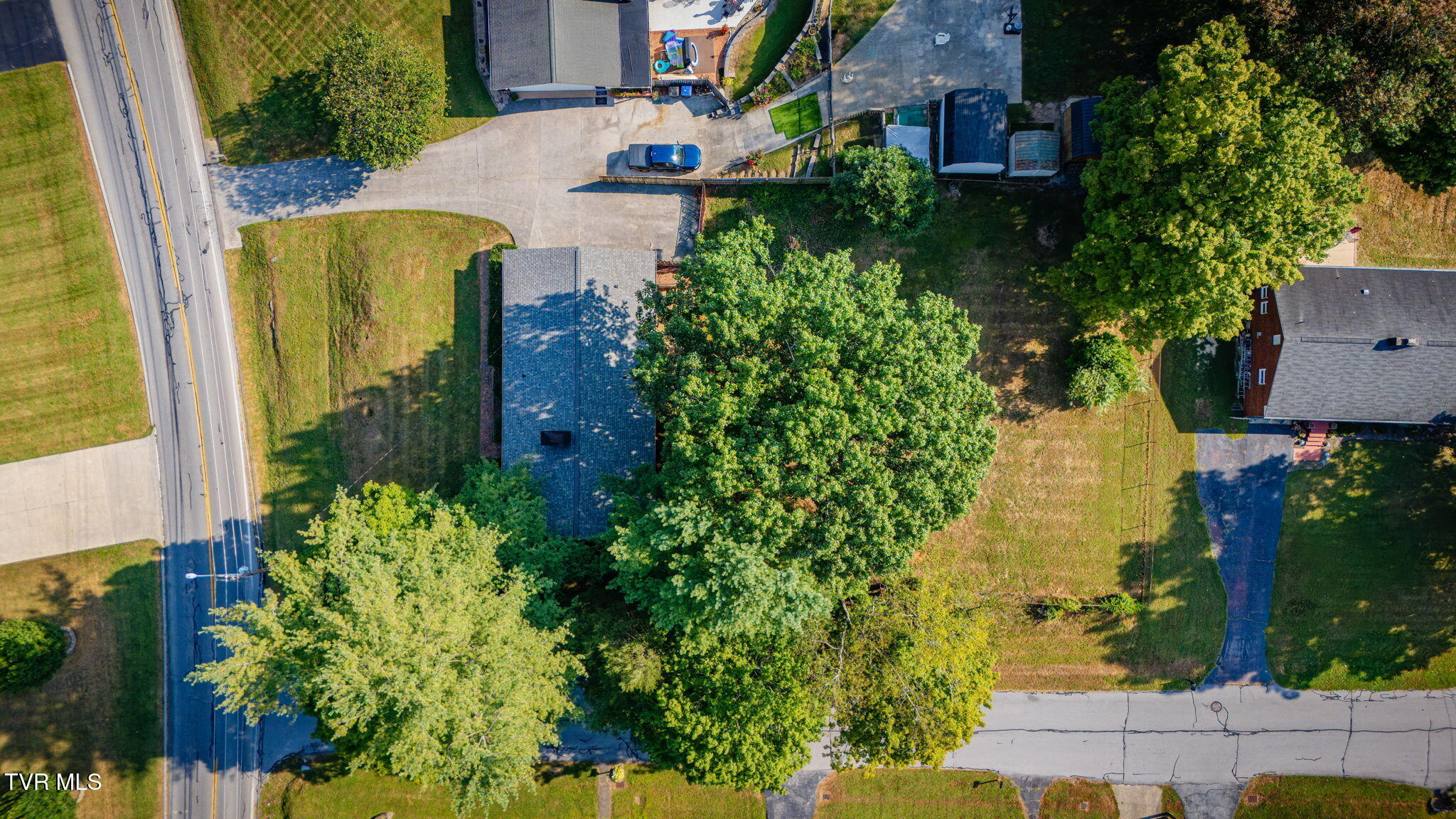 Aerial view of the home and tree-shaded grounds beside the road.