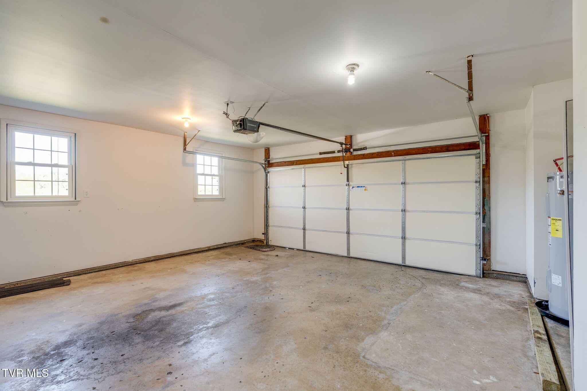 Empty garage with a concrete floor, two windows, and a large sectional overhead door.
