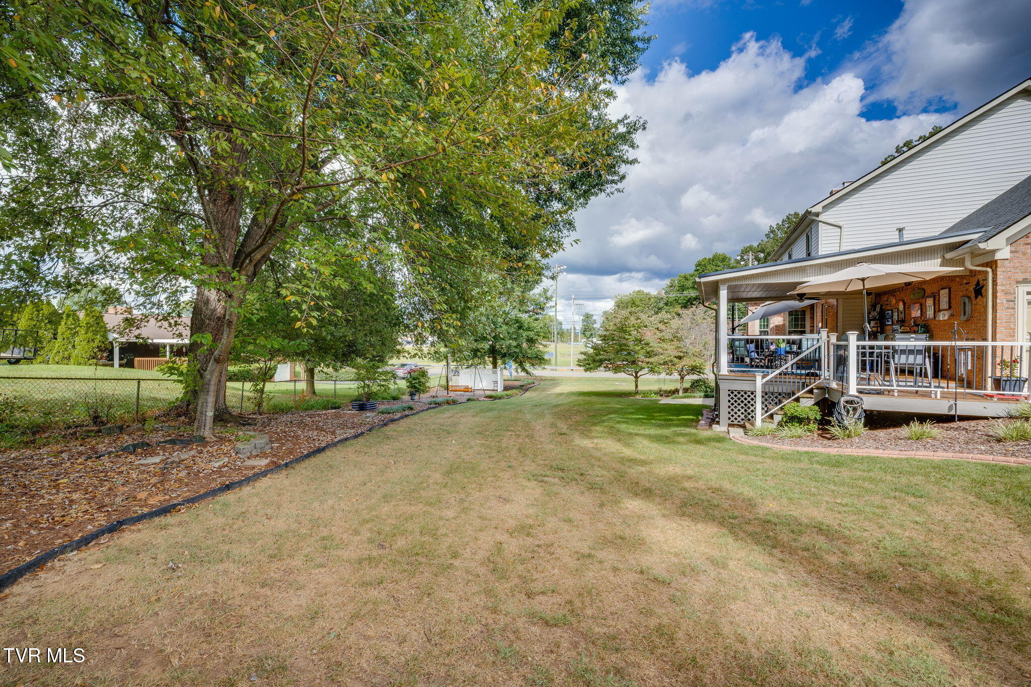 Backyard with a large shade tree, broad lawn, and covered brick patio with deck.