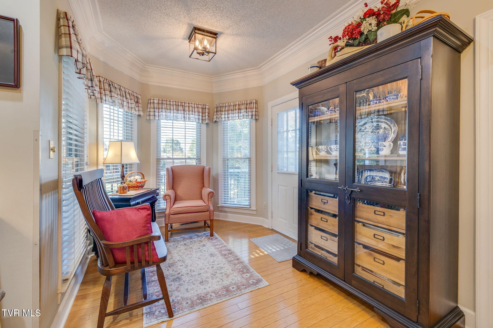 Sitting room with tall windows, two chairs, hardwood floors, and a large china cabinet.