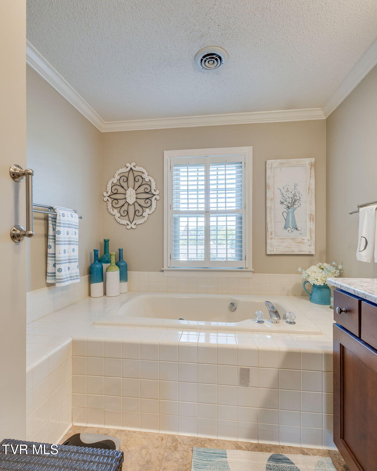 Bathroom with a tiled soaking tub beneath a shuttered window and a dark wood vanity.