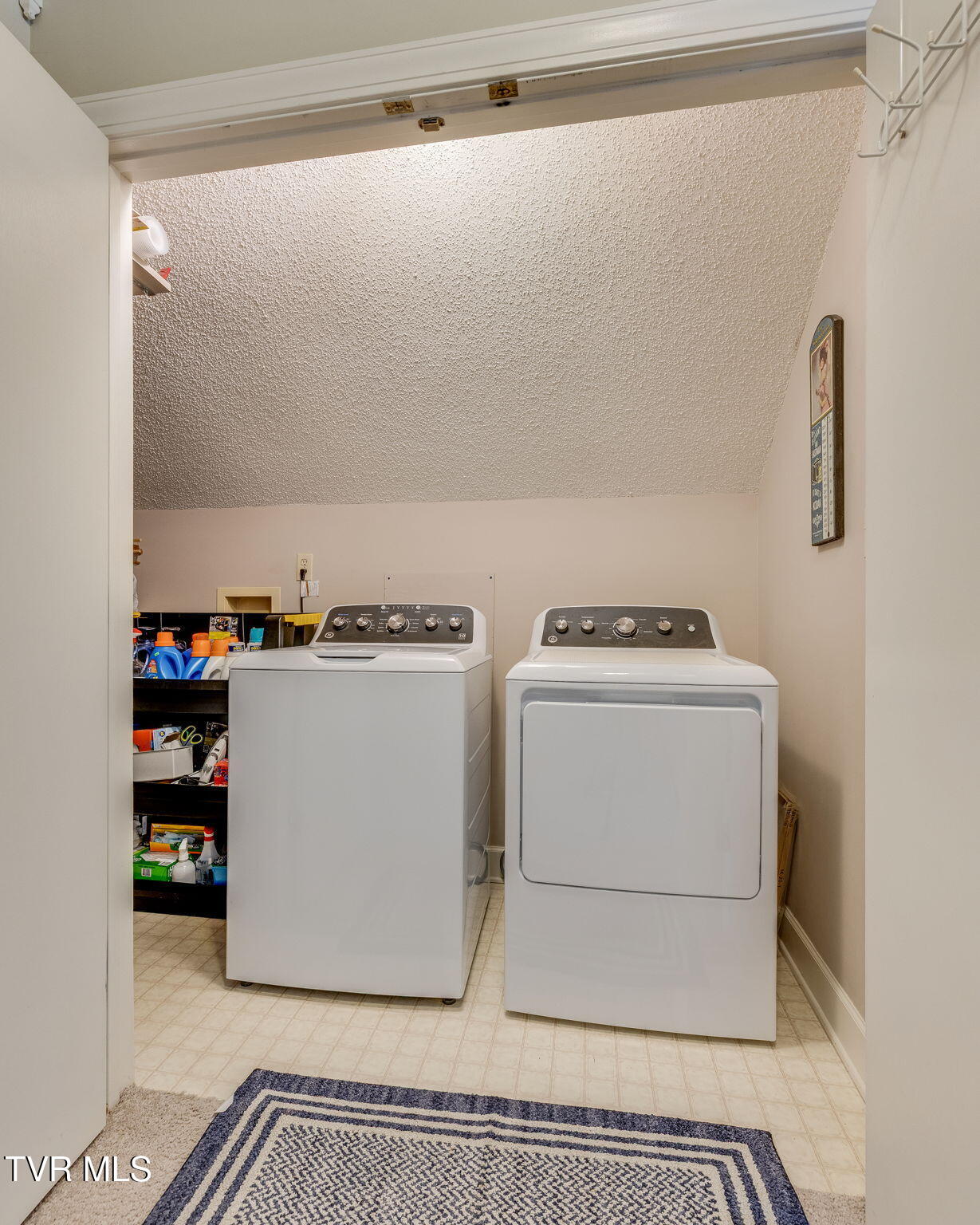 Laundry room with a top-loading washer, front-loading dryer, and open shelving.