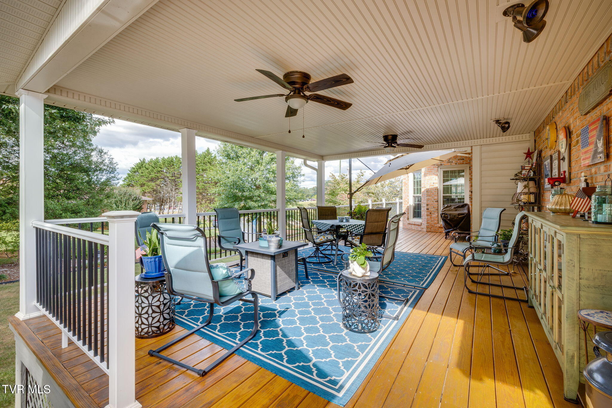 Covered porch with ceiling fans, blue rugs, outdoor seating and a dining area.