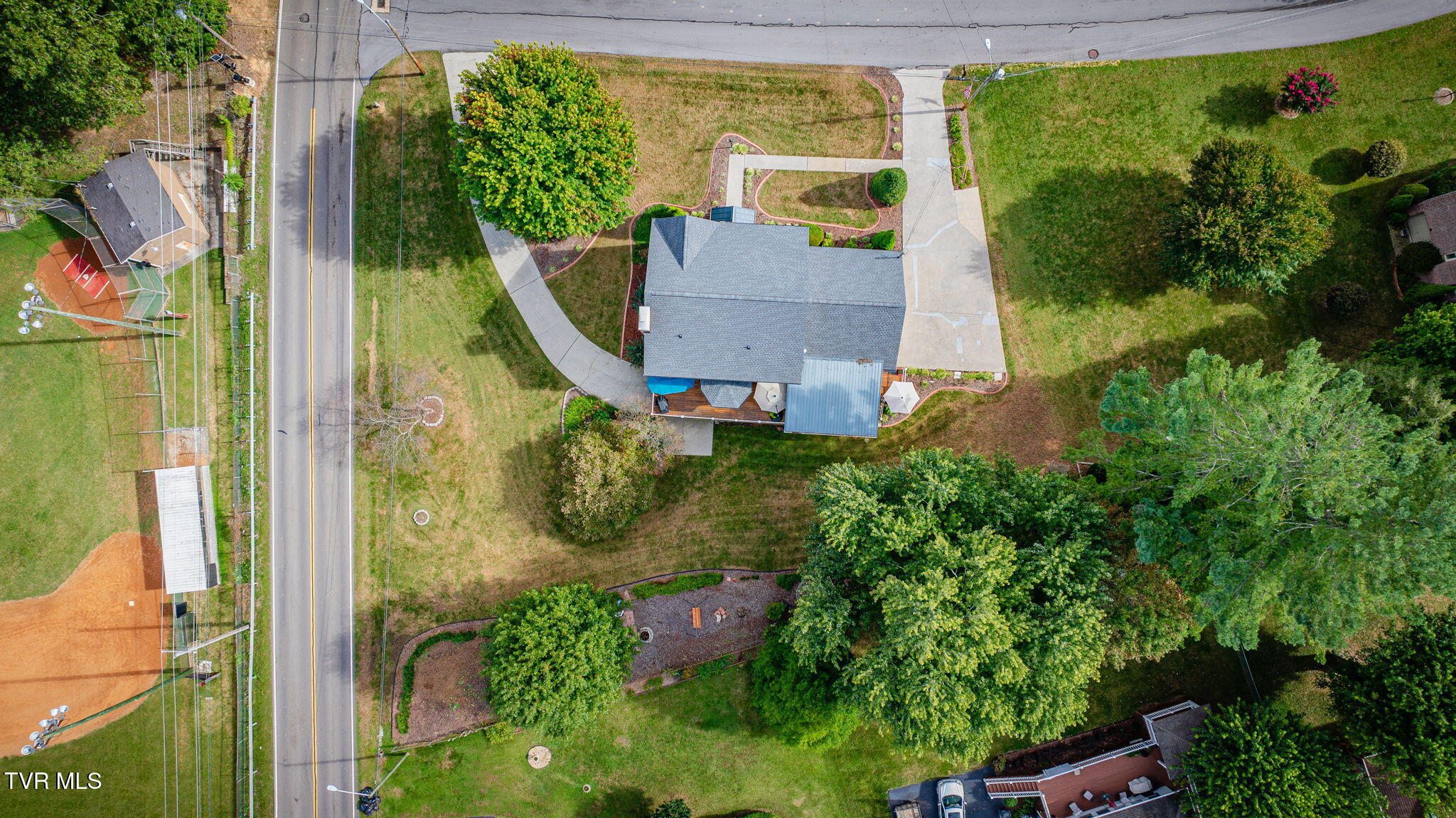 Aerial view of a home with landscaped grounds, curved walkways, and a broad driveway.