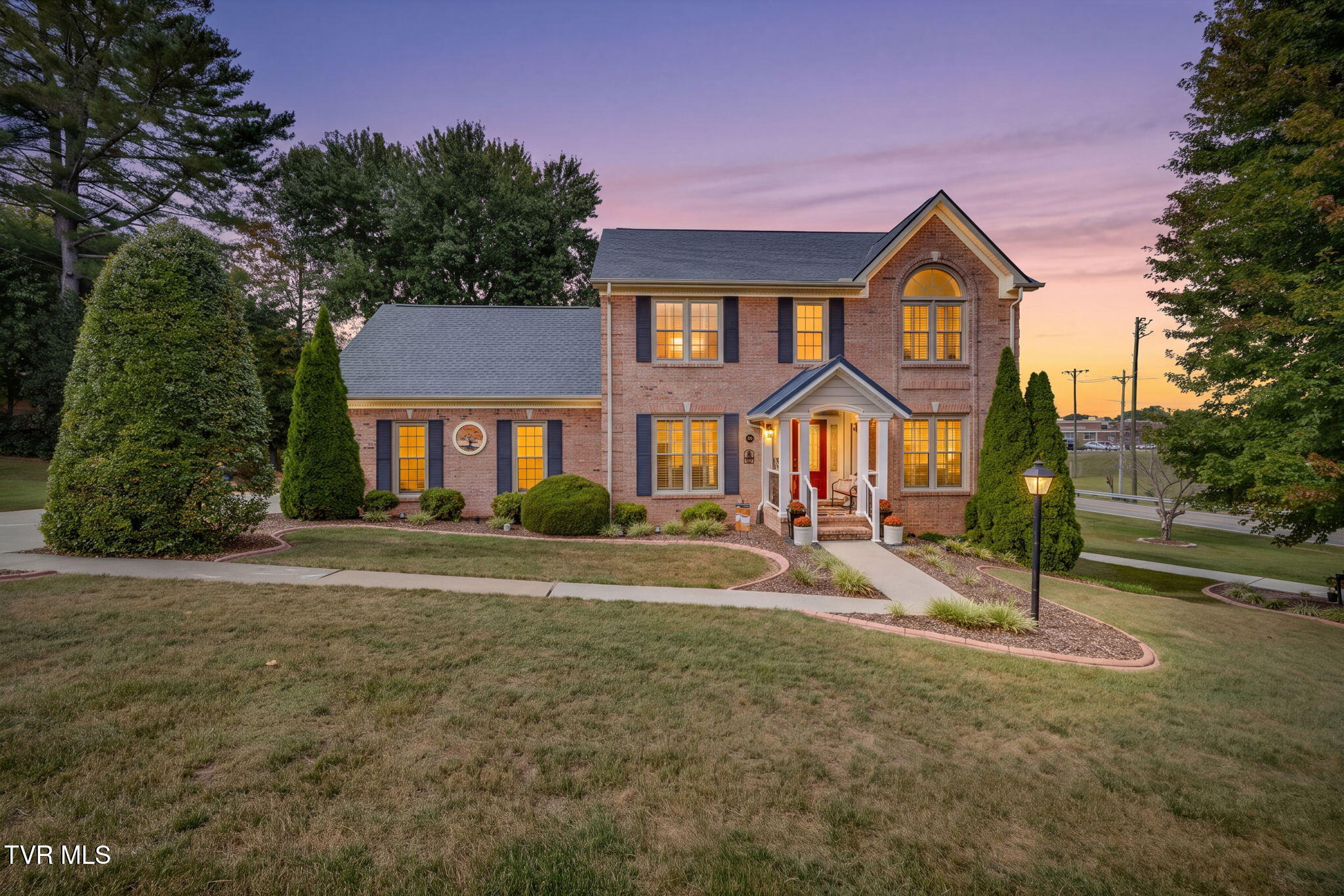 Two-story brick home with a covered entry and arched window, photographed at dusk.