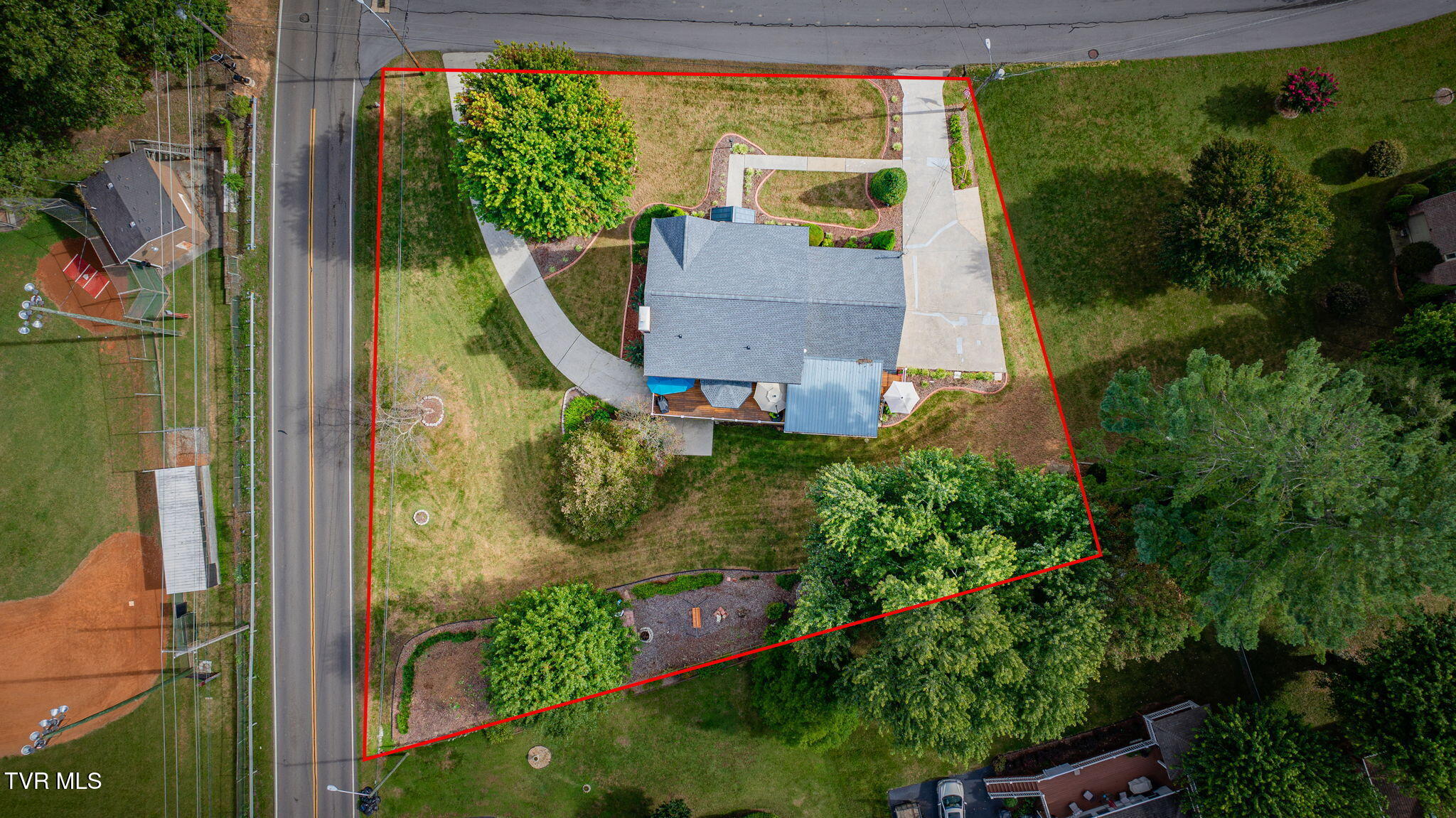 Aerial view of a home and landscaped lot outlined in red, with a large driveway and mature trees.