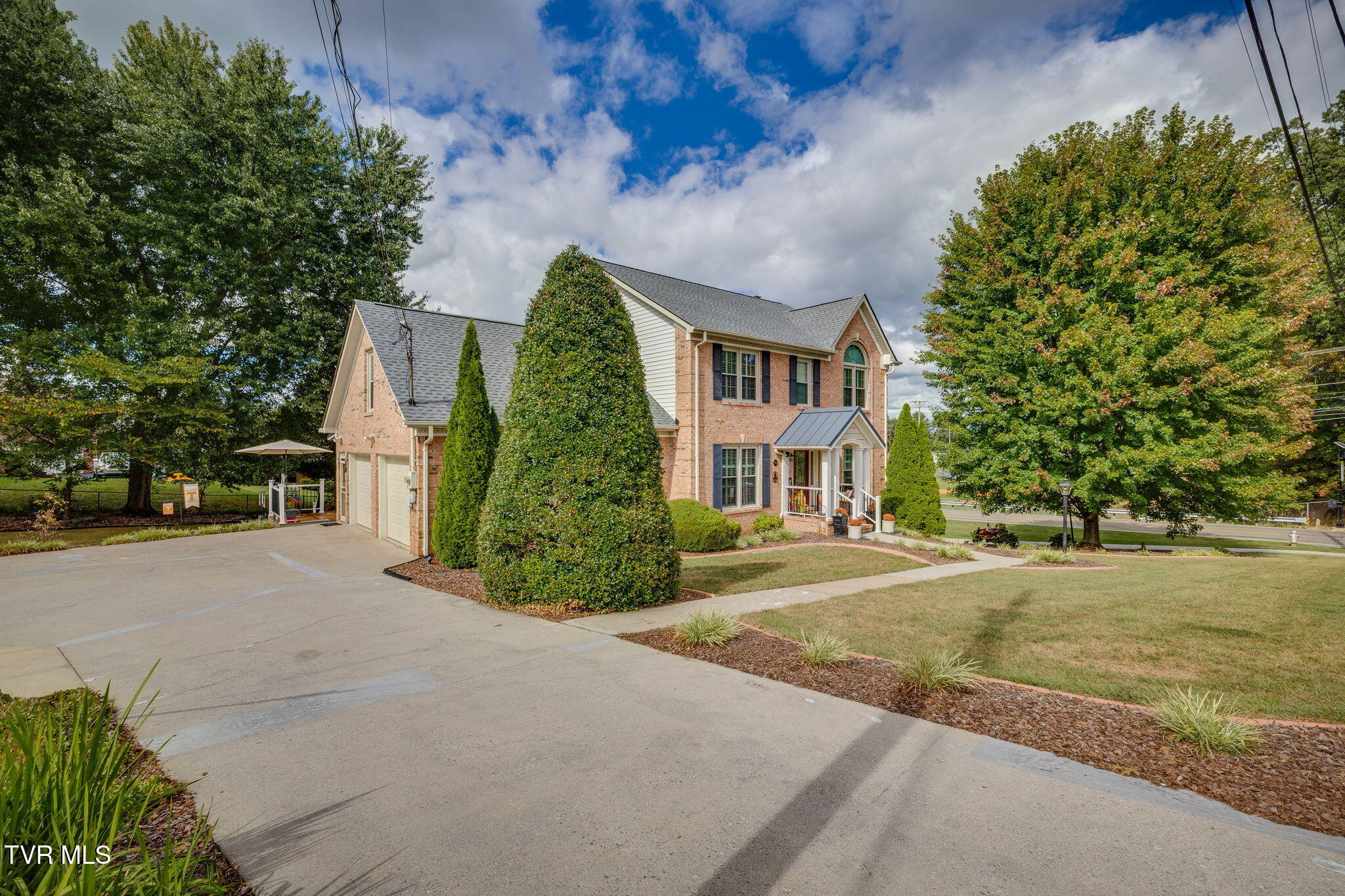 Two-story brick house with an attached garage, landscaped lawn, and broad concrete driveway.