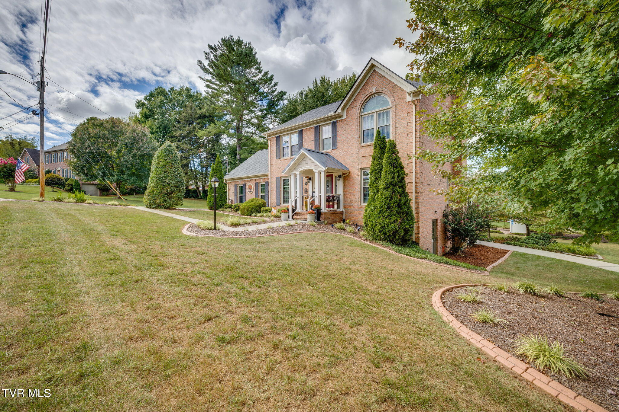Two-story brick house with a covered entrance, arched window, and landscaped lawn.