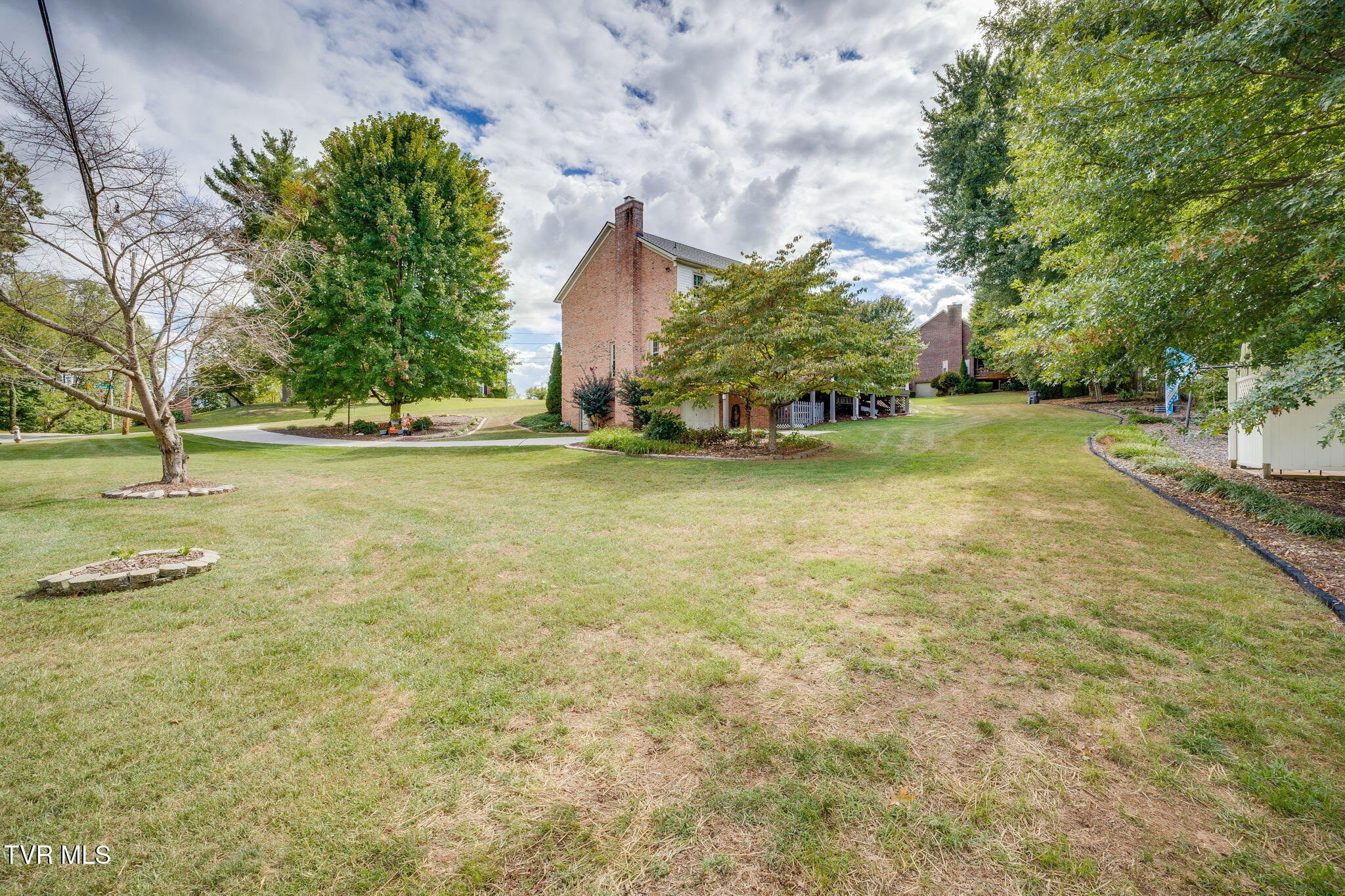 Two-story brick home beyond a broad lawn, framed by mature trees, with a covered patio below.