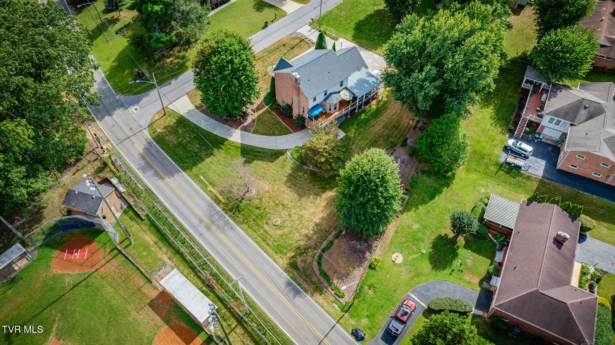 Aerial view of a two-story home with a wraparound deck and mature trees on its spacious yard.