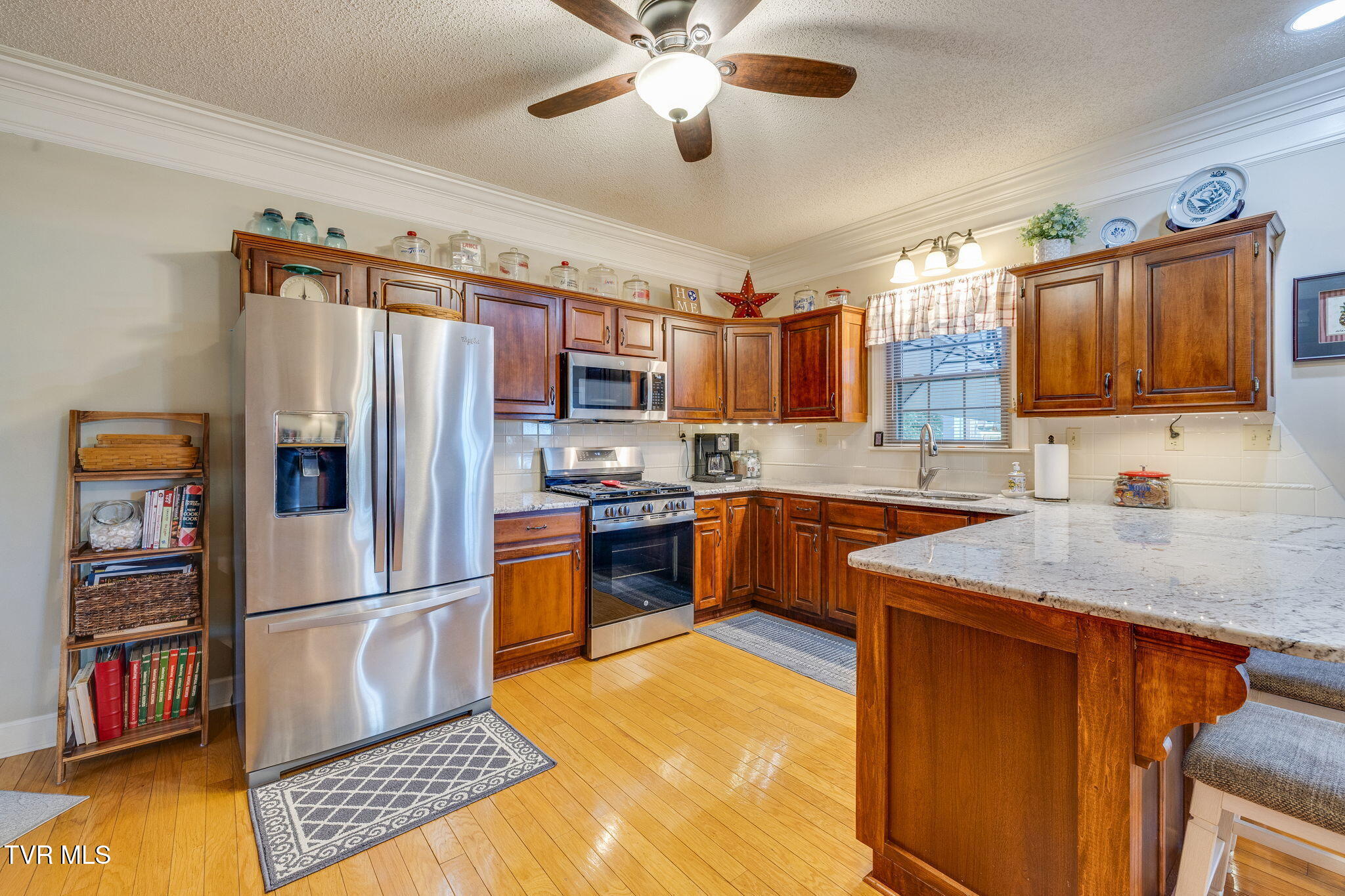 Kitchen with warm wood cabinets, stainless-steel appliances, hardwood floors, and a large granite-topped island.