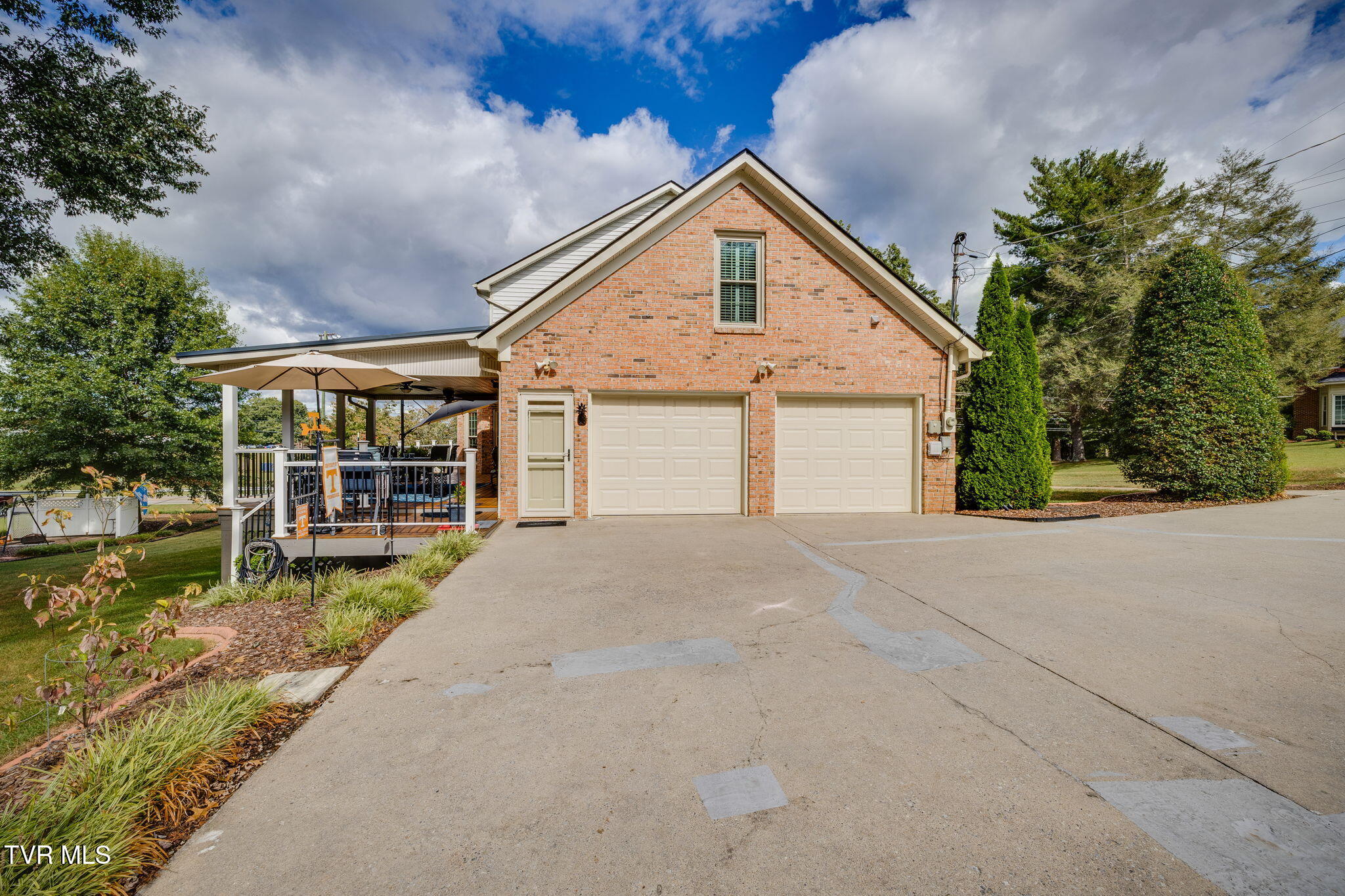 Brick house with two garage doors, a broad driveway, and a covered patio with seating.