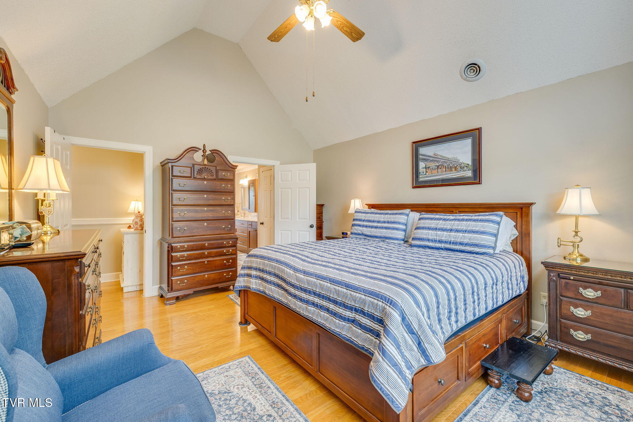 Bedroom with a wooden bed, blue striped bedding, matching dressers, and a vaulted ceiling.