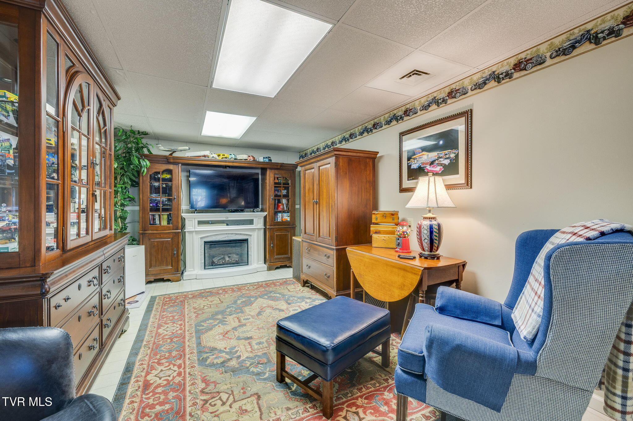 Living room with a white fireplace, wood cabinetry, blue armchair, and patterned rug.