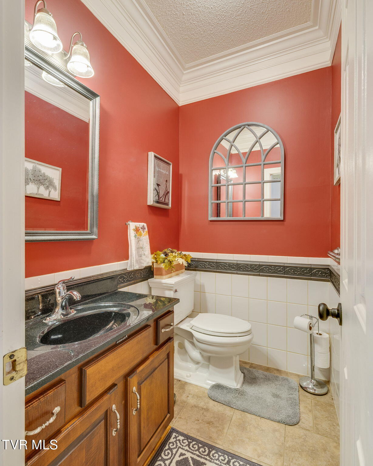 Bathroom with red walls, a wood vanity, white tile wainscoting, and an arched mirror.