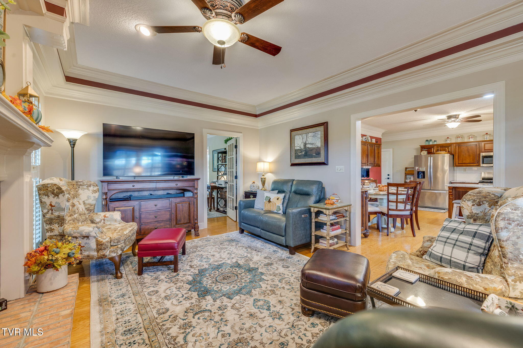 Living room with a fireplace, blue loveseat, patterned armchairs, and open kitchen beyond.
