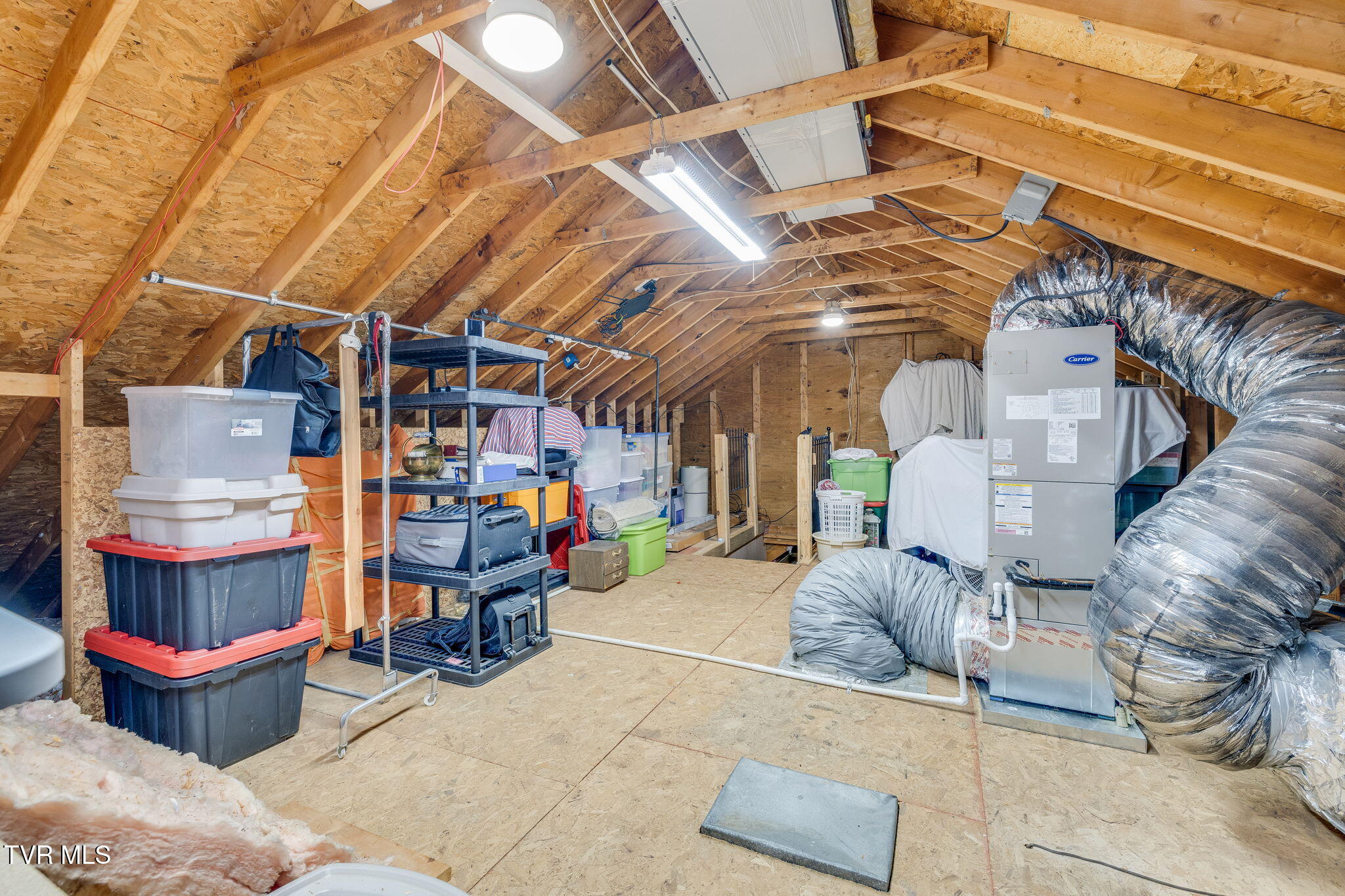 Unfinished attic with exposed rafters, storage shelving, and a large HVAC system.