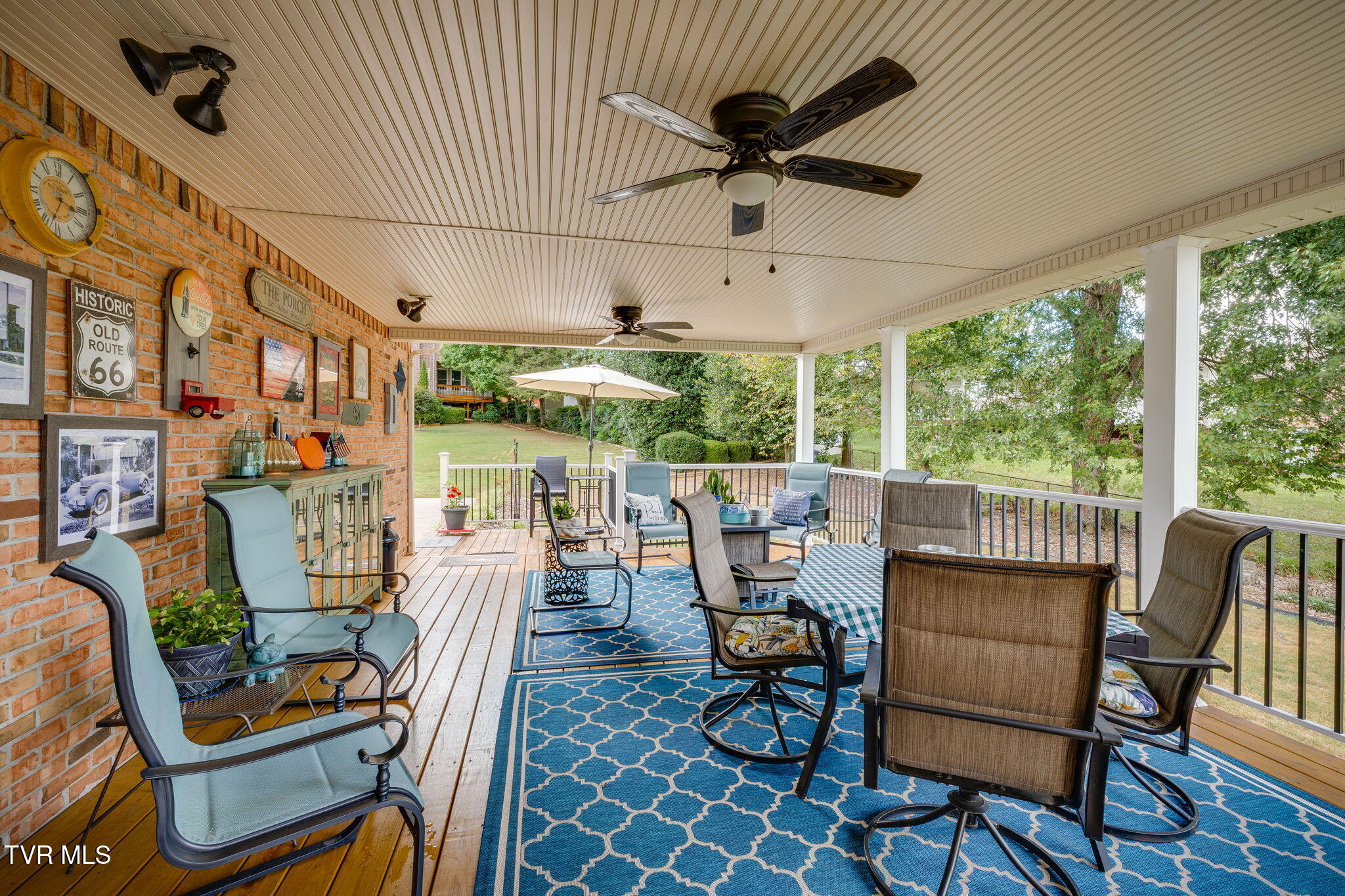 Covered porch with ceiling fans, brick wall, and seating arranged on blue patterned rugs.
