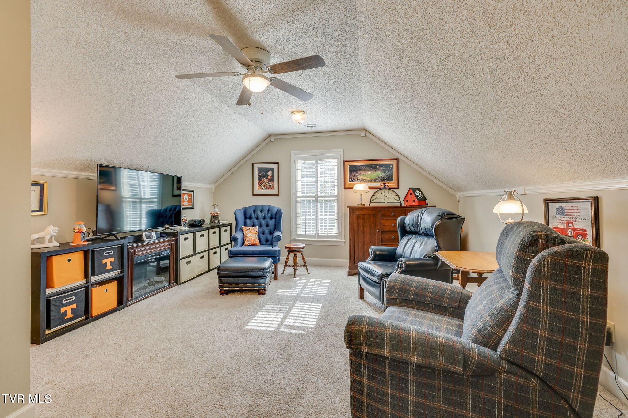 Attic bonus room with a television, blue armchair, plaid recliners, and daylight through shuttered window.