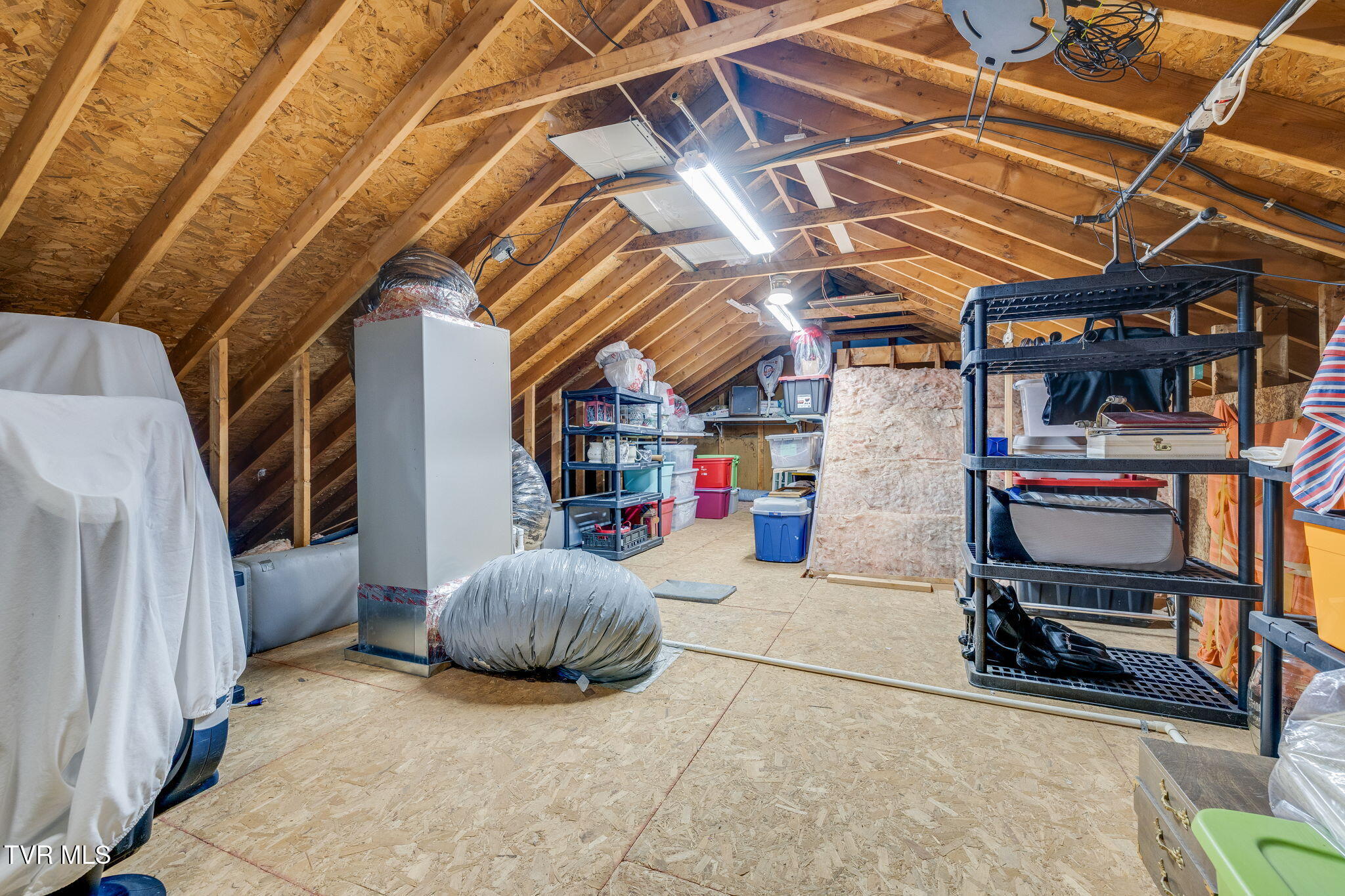 Unfinished attic storage space with exposed rafters, HVAC equipment, and shelving.
