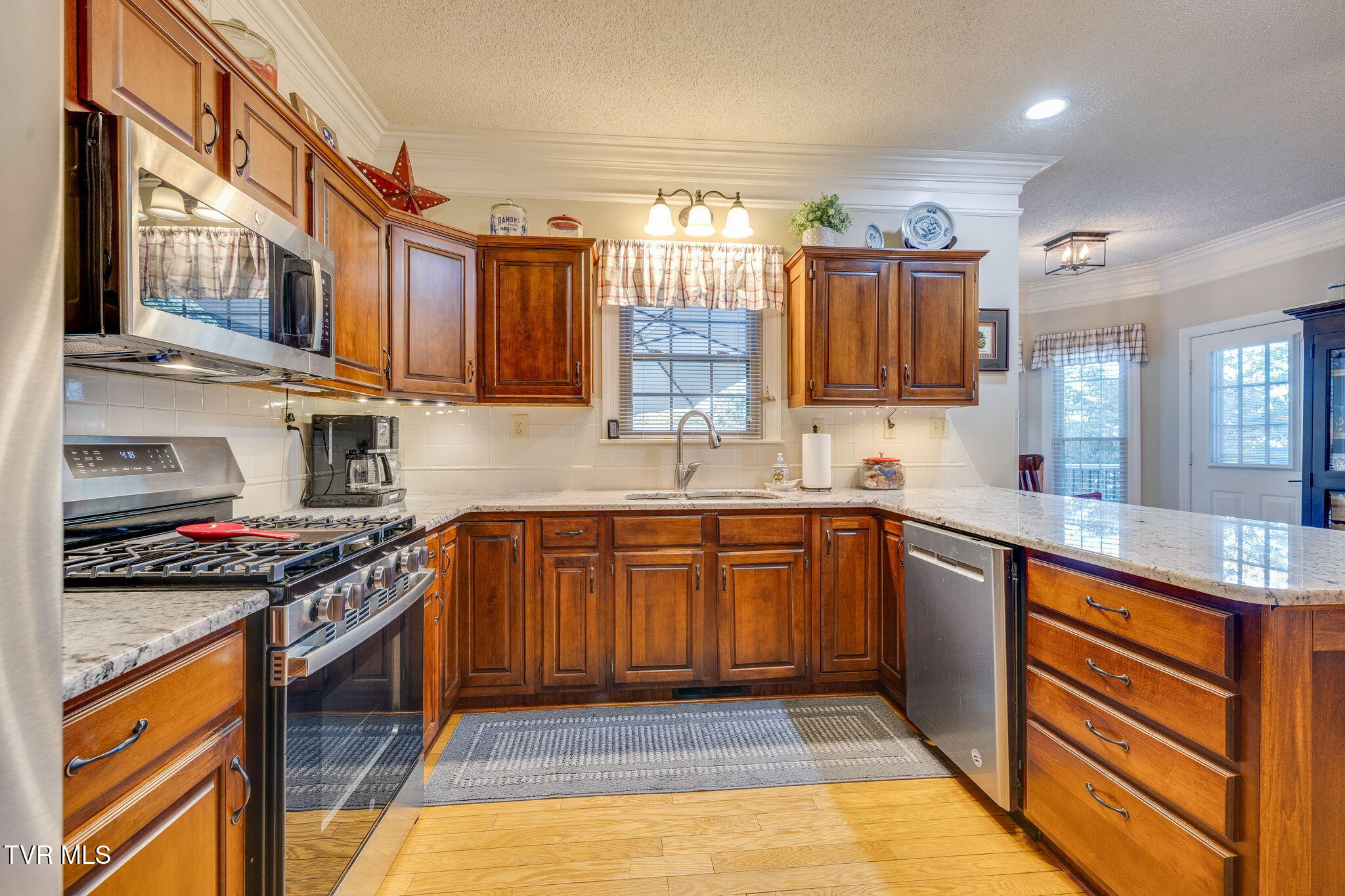 Kitchen with warm wood cabinetry, granite counters, and stainless-steel appliances.