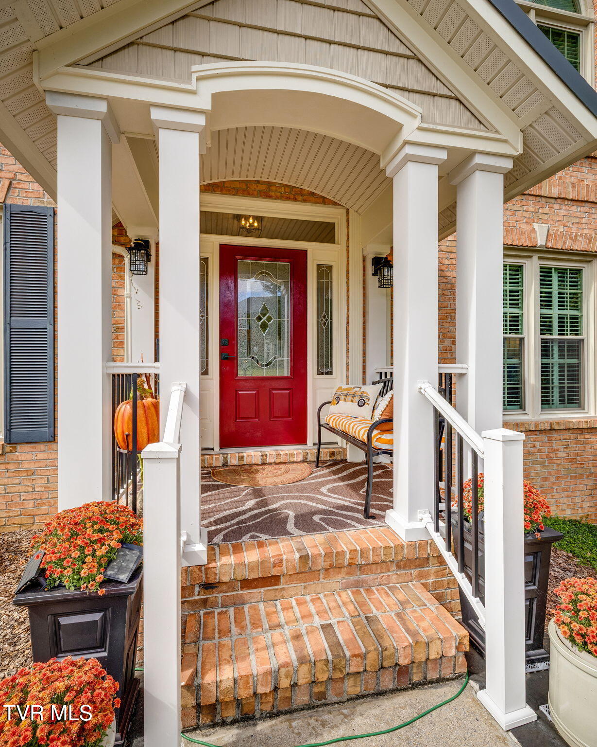 Brick home’s covered front porch with white columns, brick steps, and a distinctive red glass-paneled door.