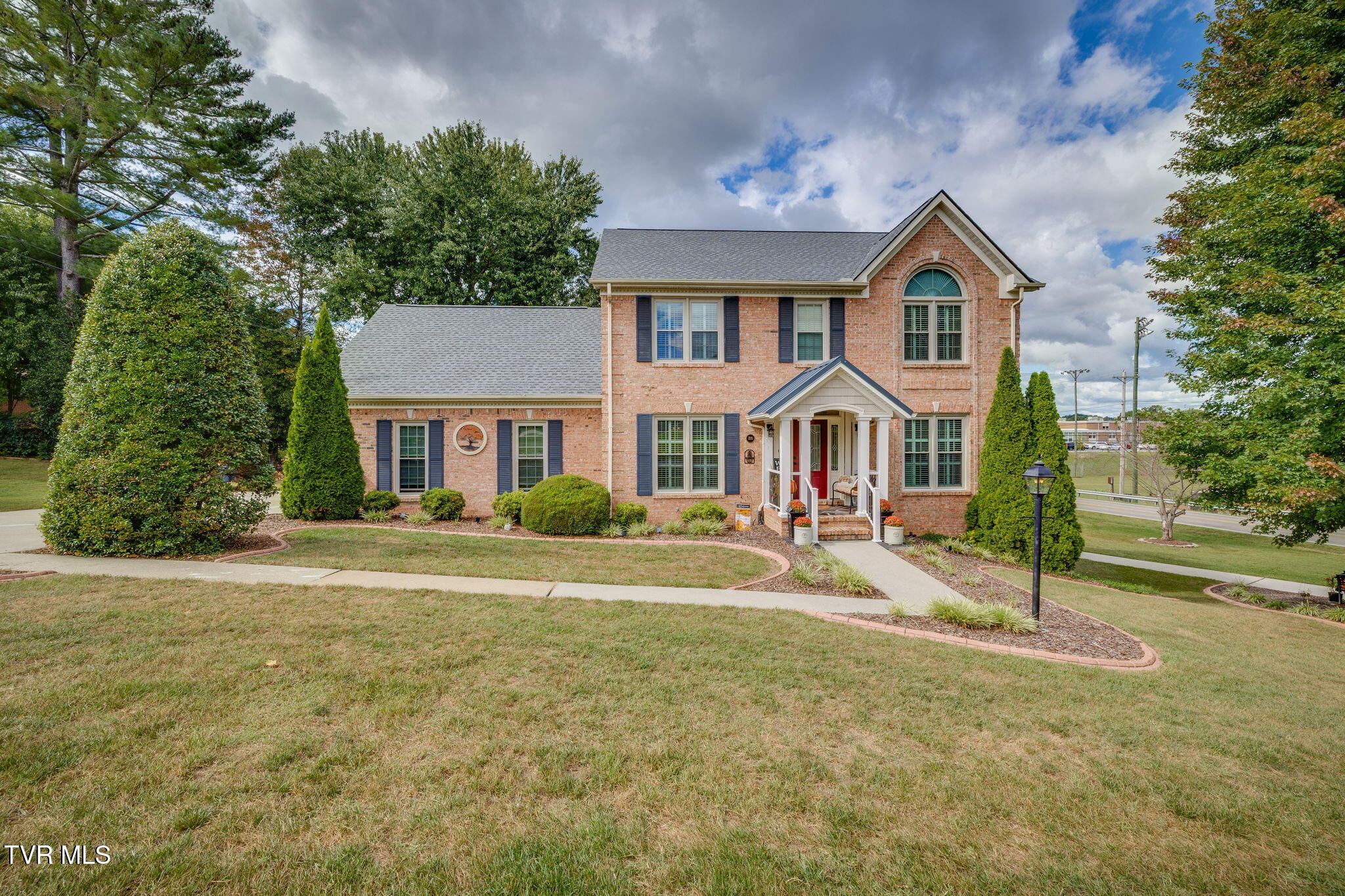 Two-story brick house with an arched upper window, covered porch, and landscaped front lawn.