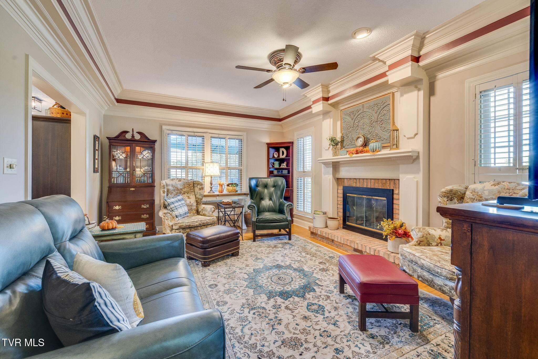 Furnished living room with a brick fireplace, ornate mantel, and large patterned rug.