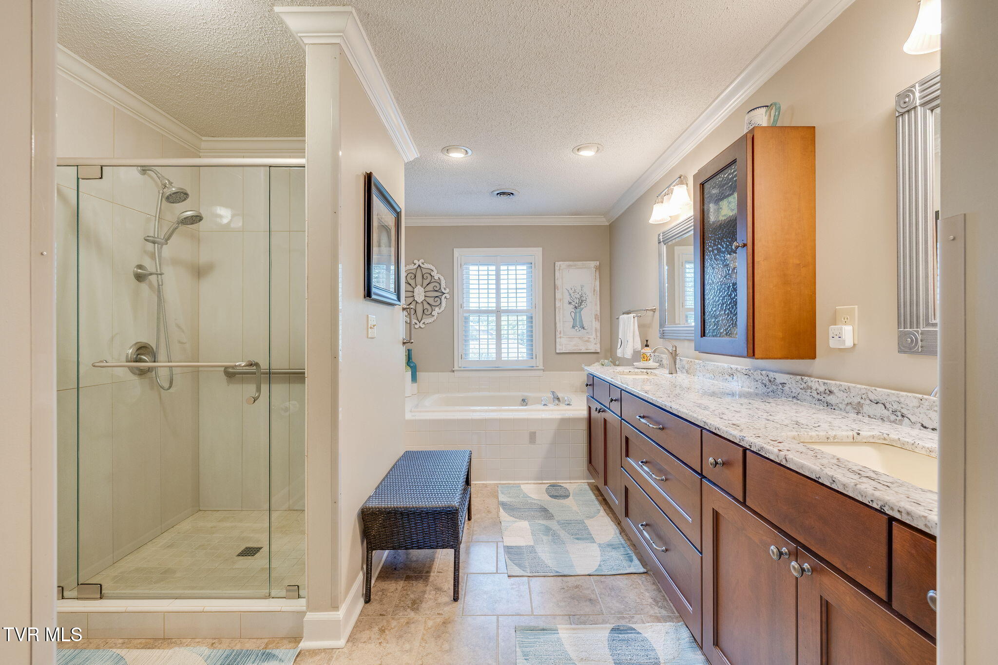 Bathroom with a glass walk-in shower, a bathtub beneath a shuttered window, and a long granite-topped vanity.