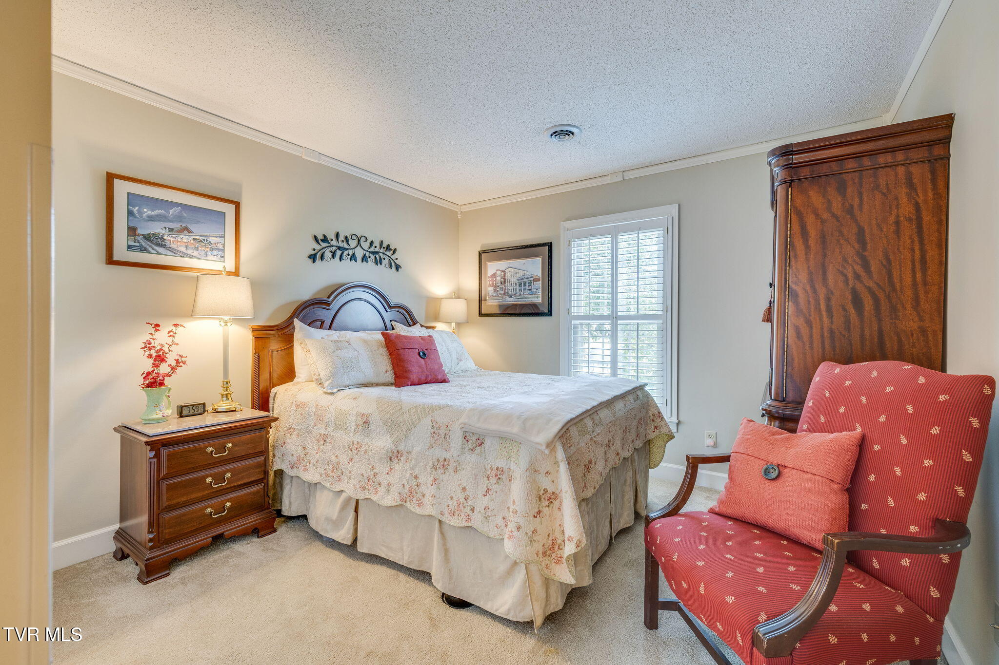 Bedroom with a floral-covered bed, dark wood furniture, and a red upholstered armchair.
