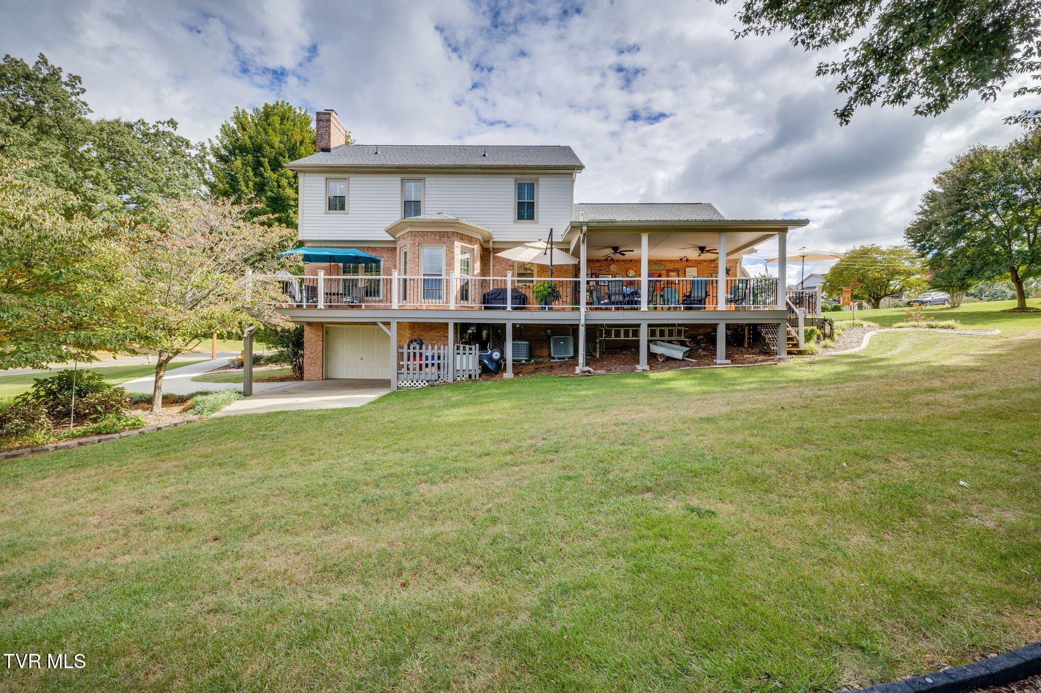 Two-story home with a large elevated deck, covered patio, and broad lawn.