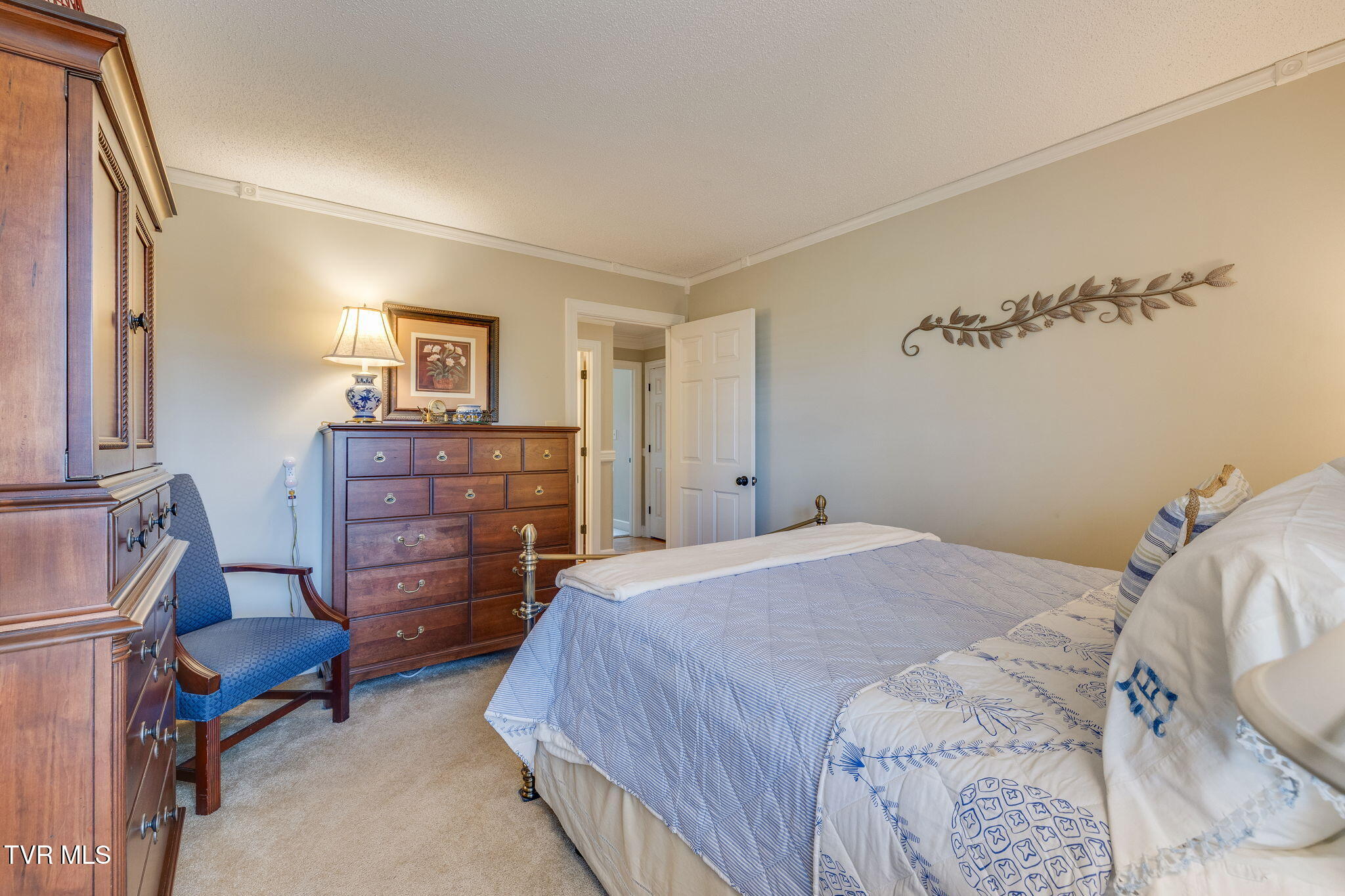 Furnished bedroom with blue-and-white bedding, wooden dressers, and a blue upholstered chair.