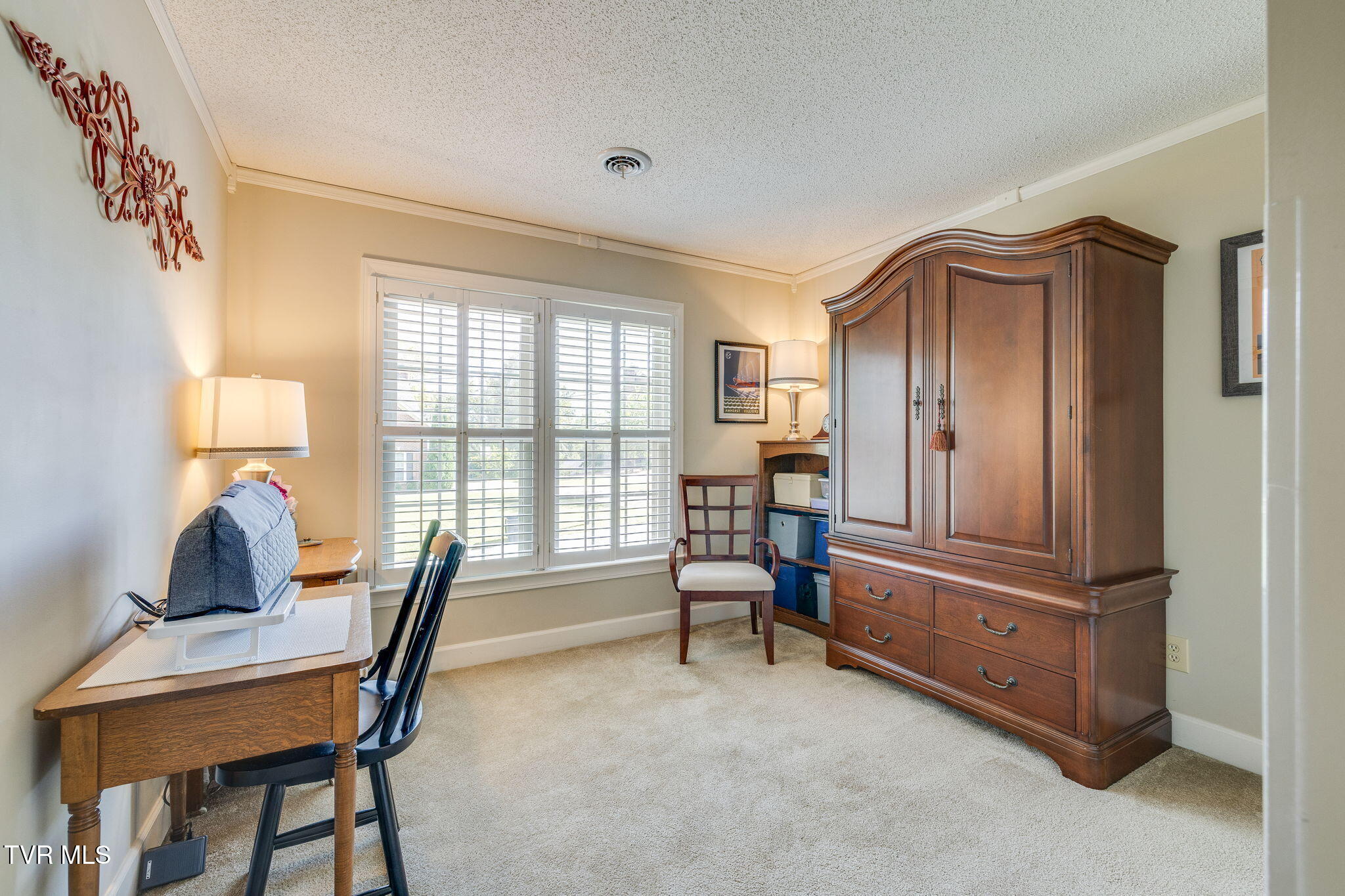Furnished home office with a large wooden armoire and wide shuttered windows.