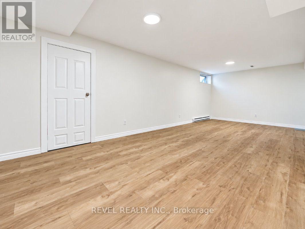 Empty finished room with wood-look flooring, recessed lights, a paneled door, and a small high-set window.