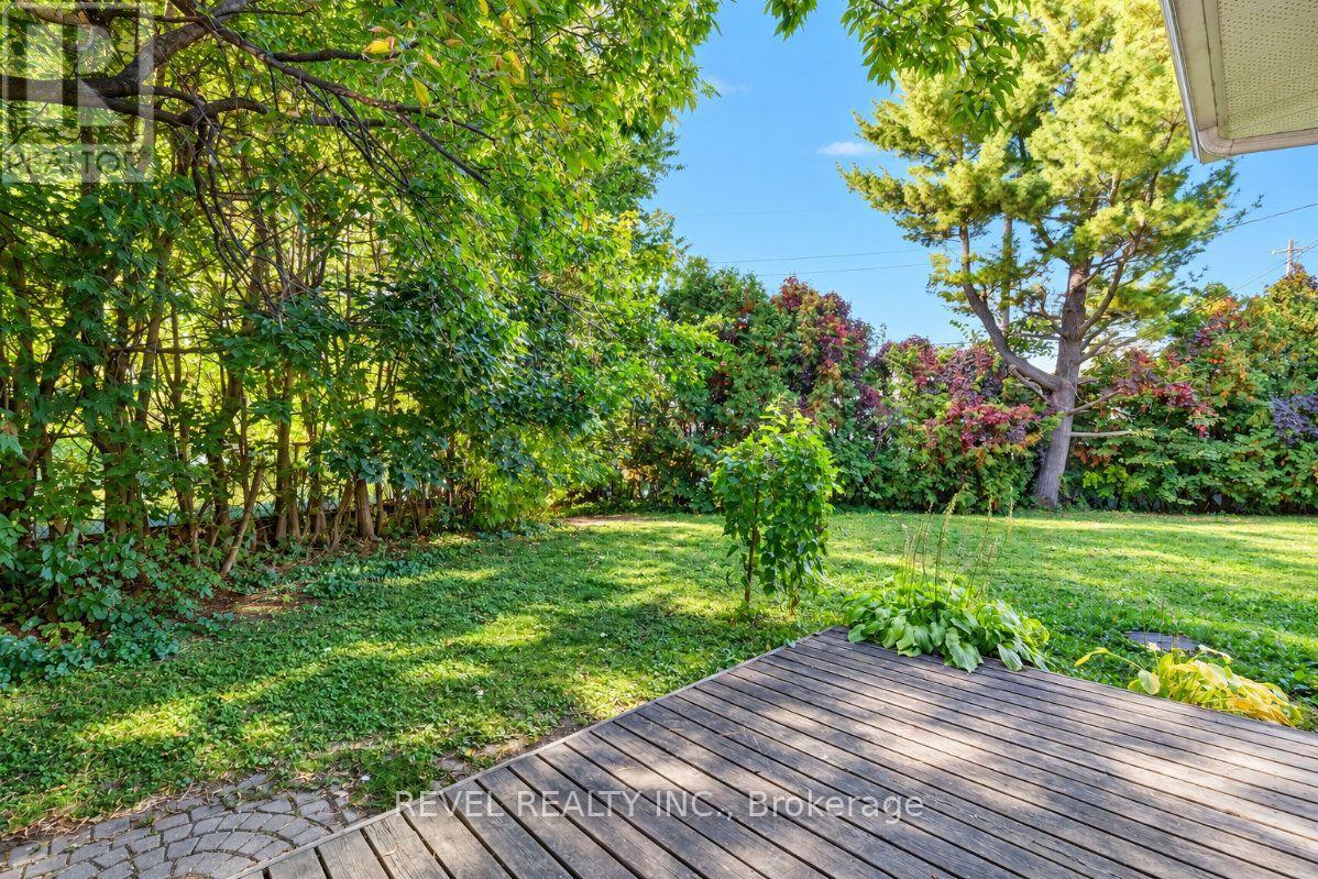 Backyard lawn bordered by mature trees and shrubs, with a wooden deck in the foreground.