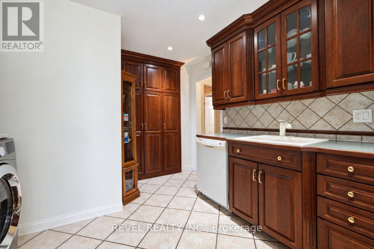 Kitchen with dark wood cabinetry, glass-front upper cabinets, tiled backsplash and white sink.