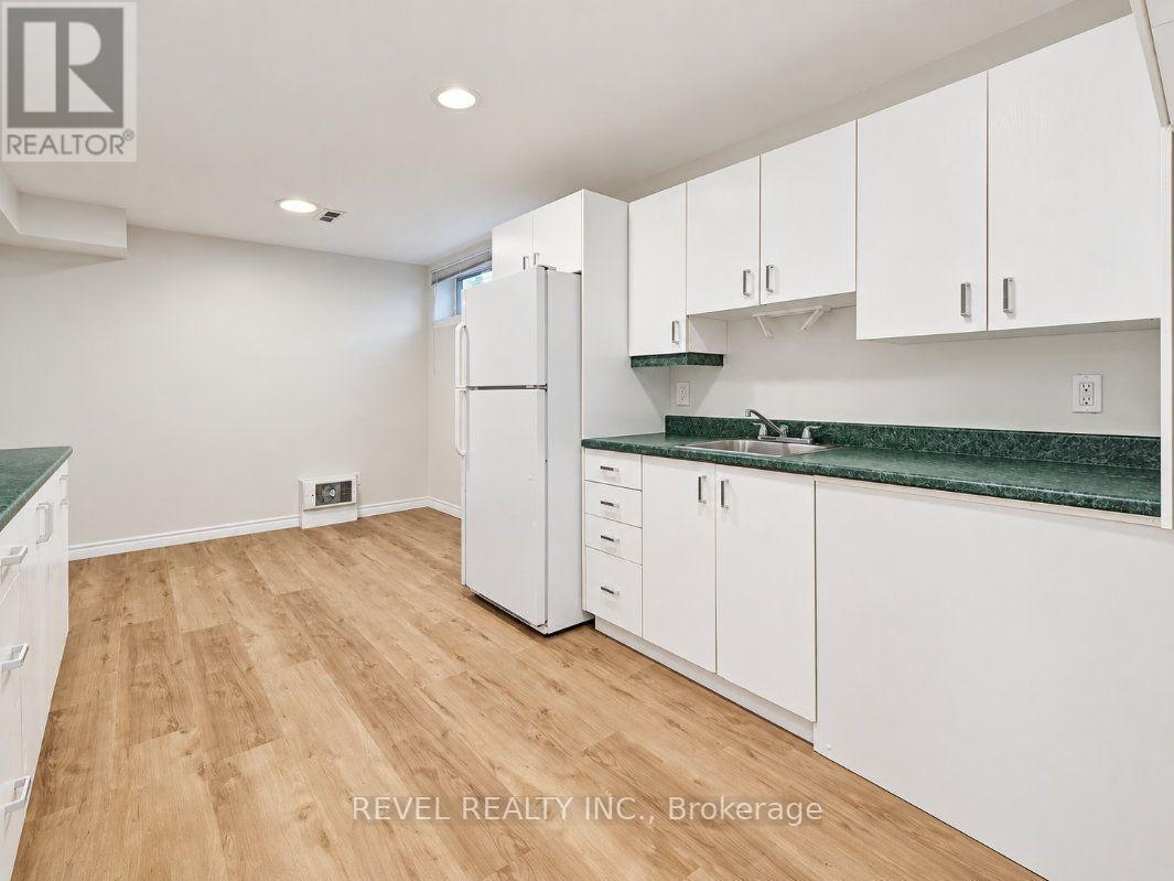 Vacant kitchen with white cabinetry, green countertops, and light wood-look flooring.