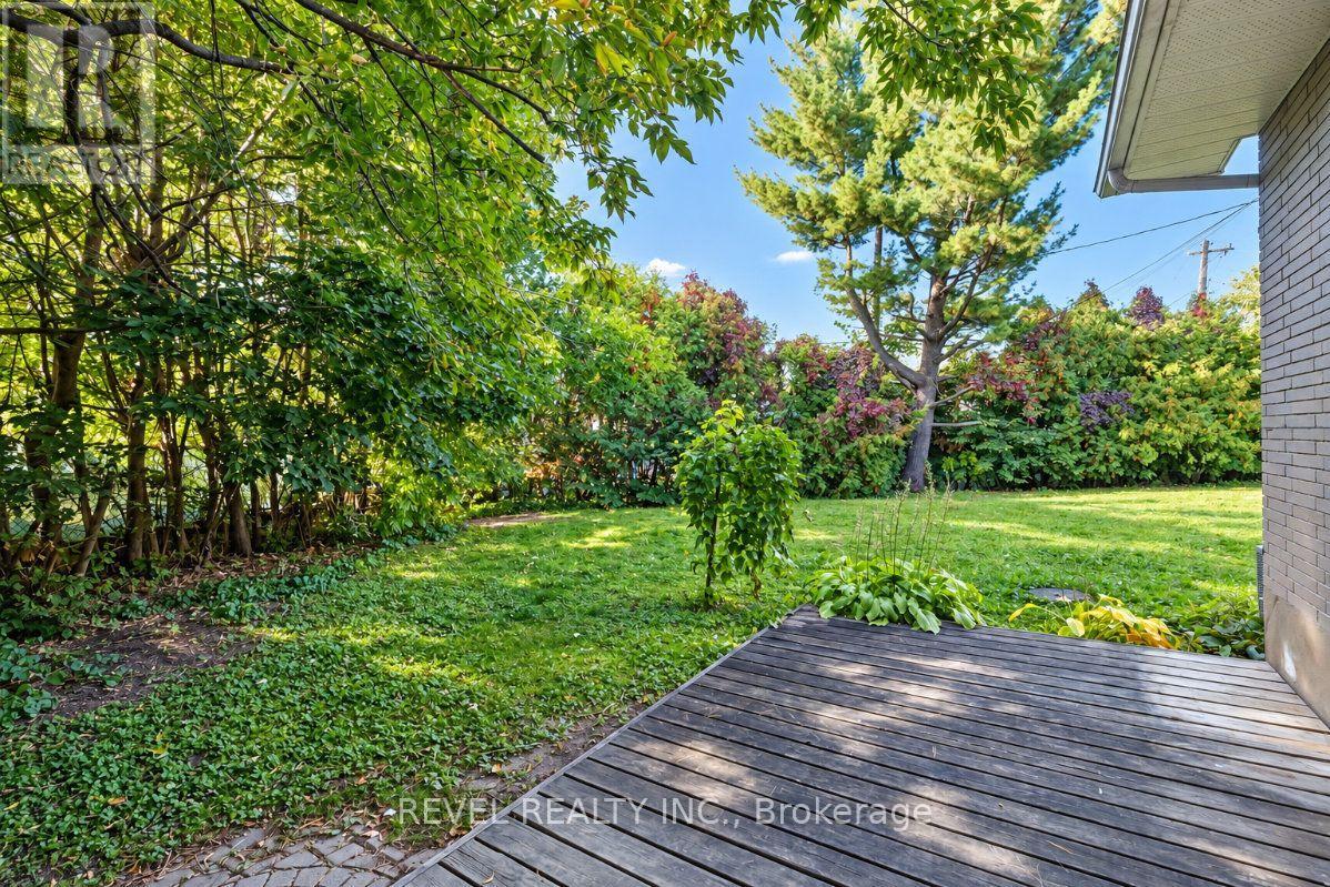 Backyard lawn bordered by mature trees and shrubs, viewed from a wooden deck.