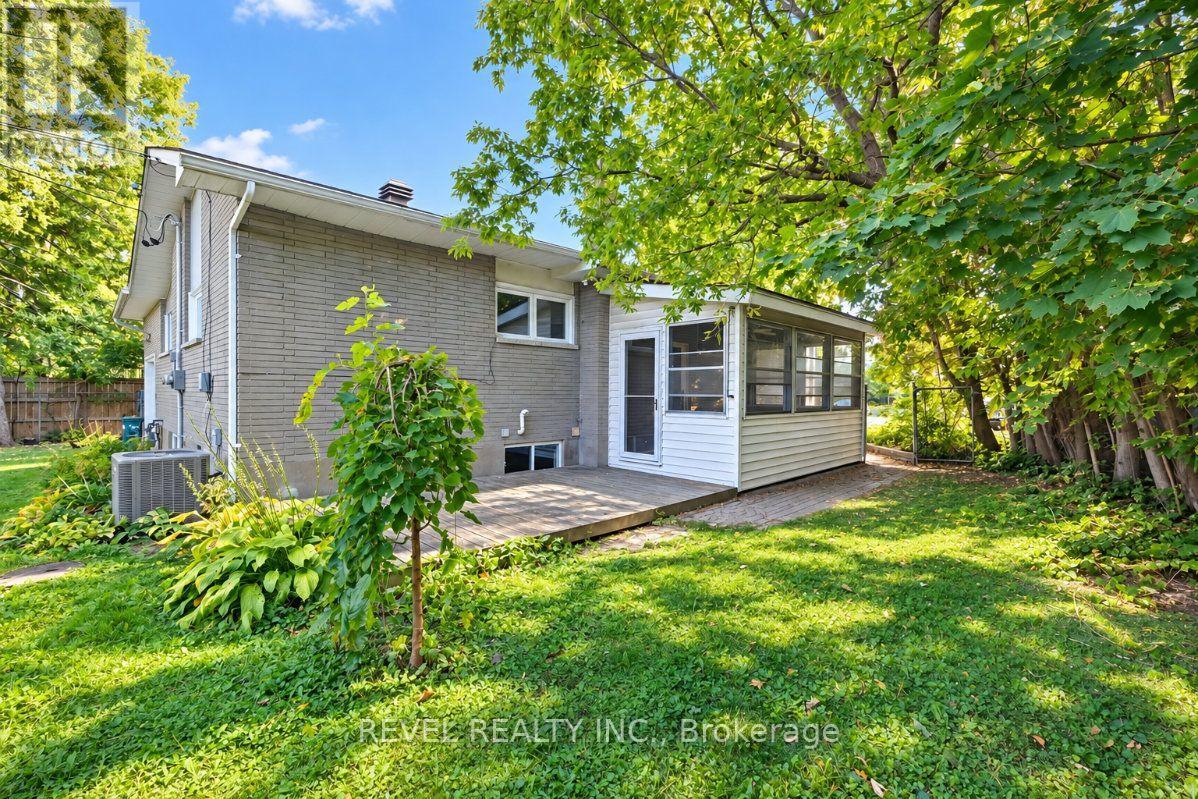 Rear exterior of a brick house with an enclosed sunroom, wooden deck, and shaded lawn.