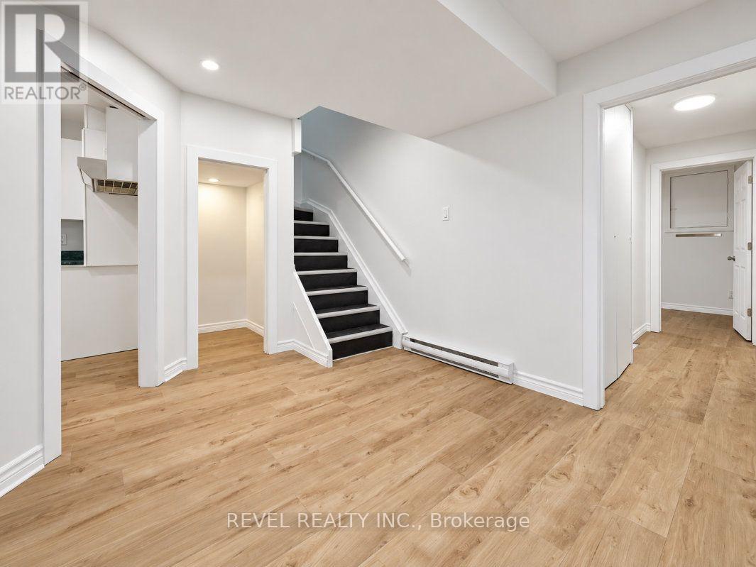 Unfurnished hallway with light wood flooring and a dark-carpeted staircase.