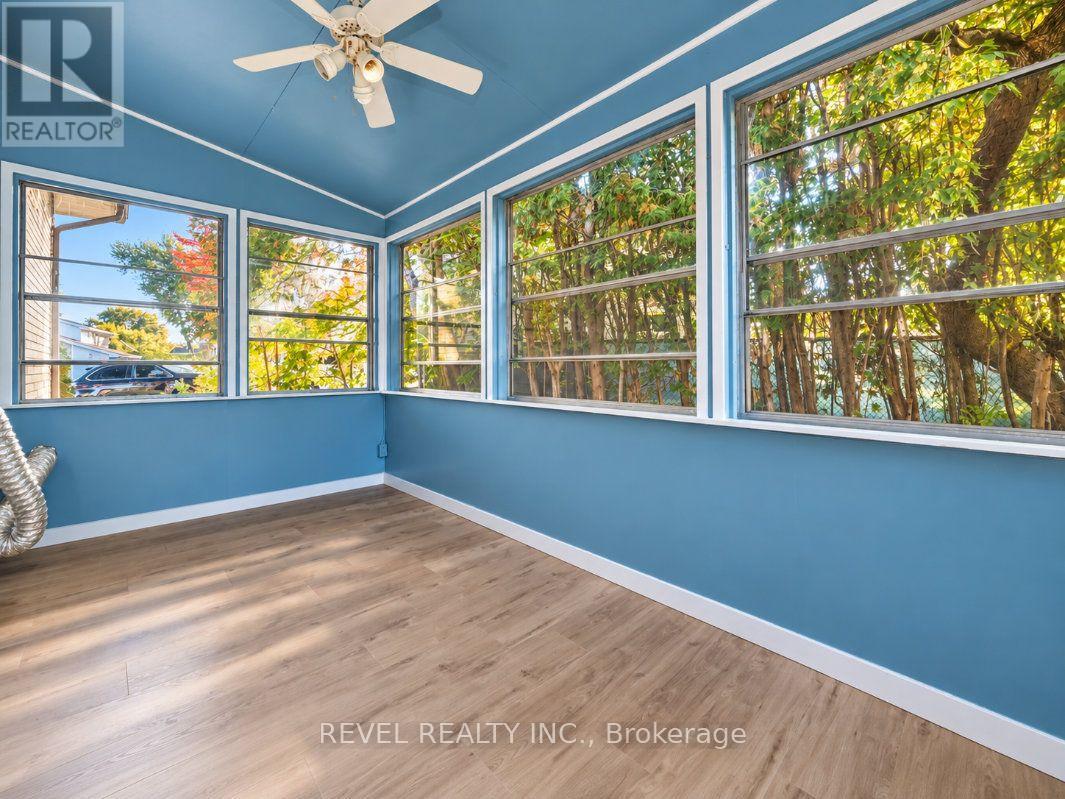 Empty sunroom with blue walls, wood-look flooring, and large windows overlooking trees.