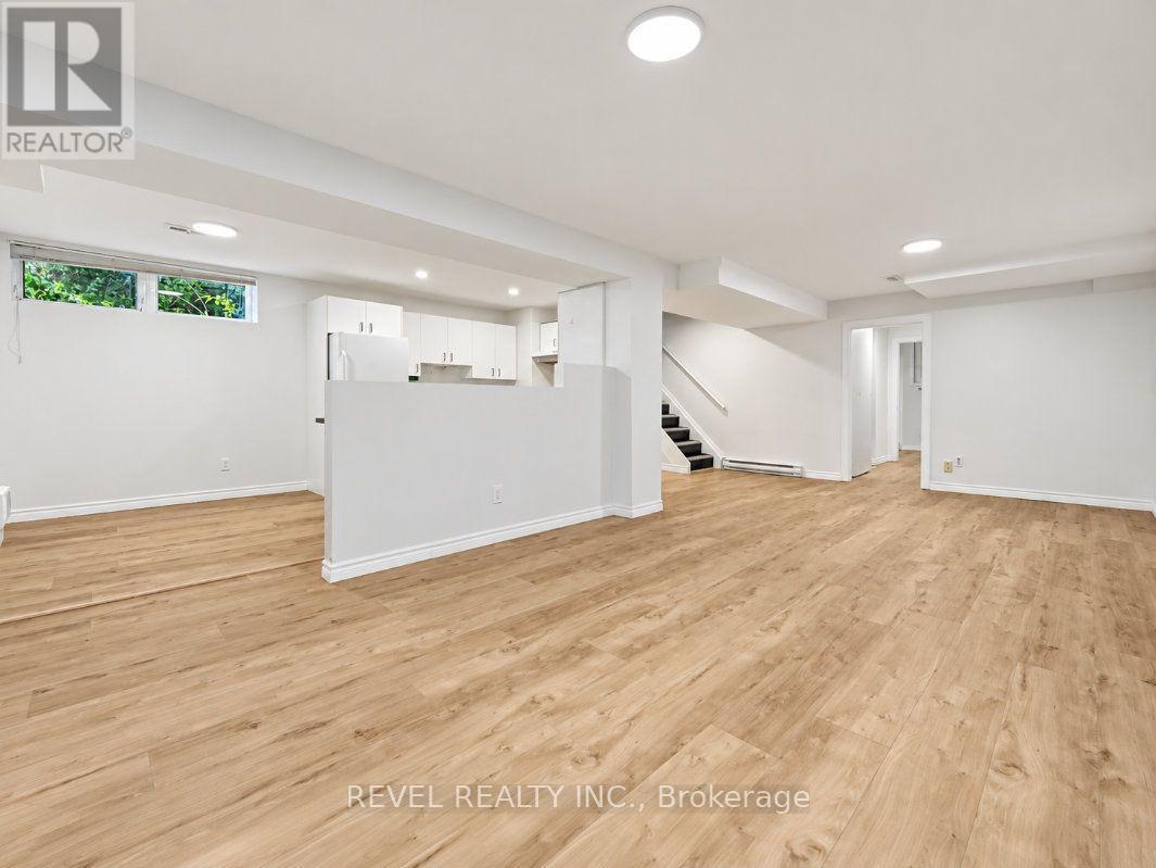 Open lower-level room with wood-look flooring, compact kitchen, and stairs.