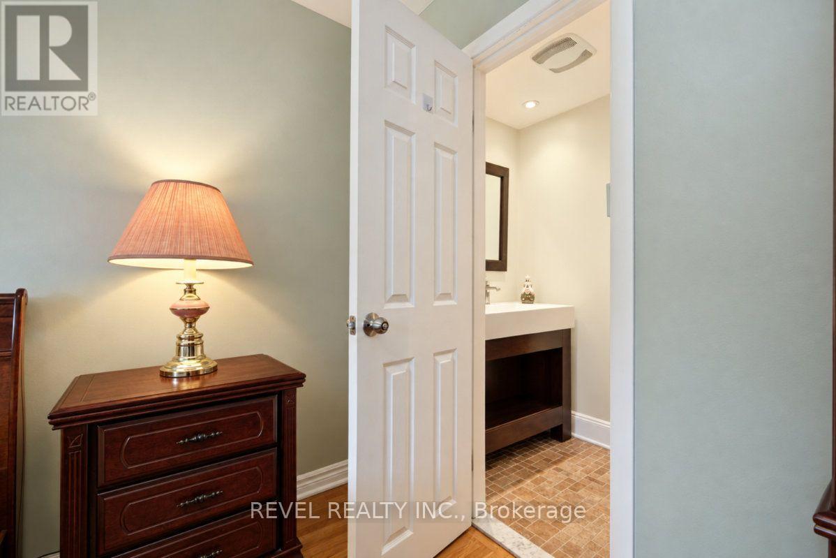 Bathroom with a dark wood vanity and tiled floor, seen through an open door beside a dresser and lamp.