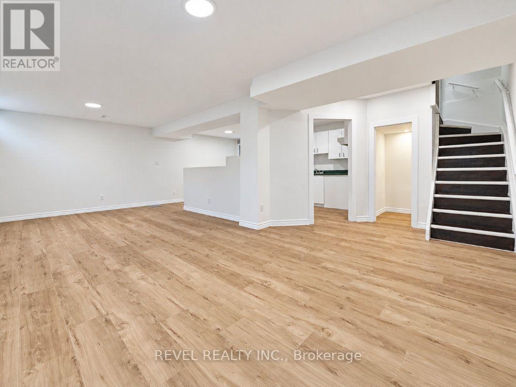 Empty finished basement with light wood-look flooring and a staircase with dark treads.