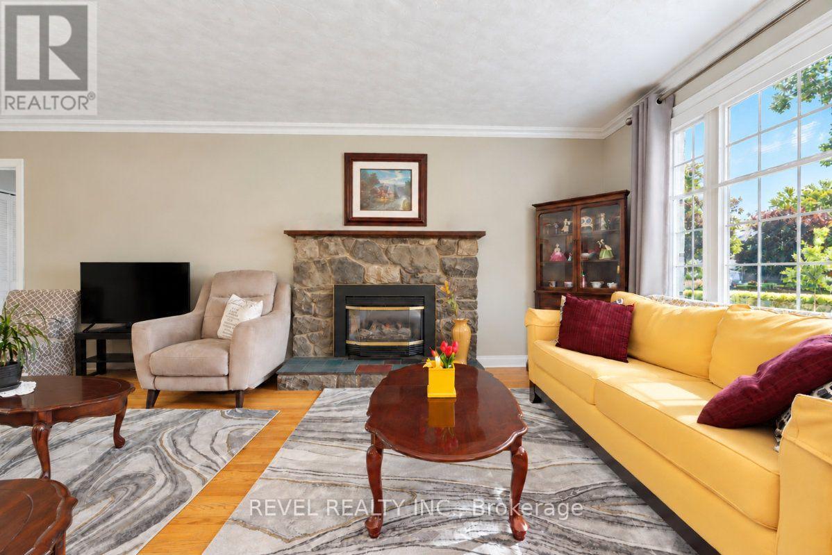 Living room with a stone fireplace, yellow sofa, and large windows overlooking greenery.